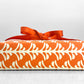 wrapping paper by Otto Editions with a cut-out palm design in white on a spice orange background. Pictured wrapped as a present with a bow