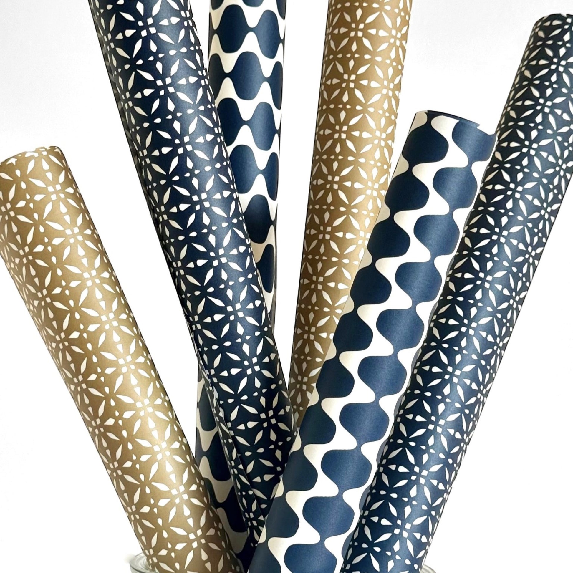wrapping paper by Otto Editions with a cut-out wavy design in white on an indigo background. Pictured rolled with other designs