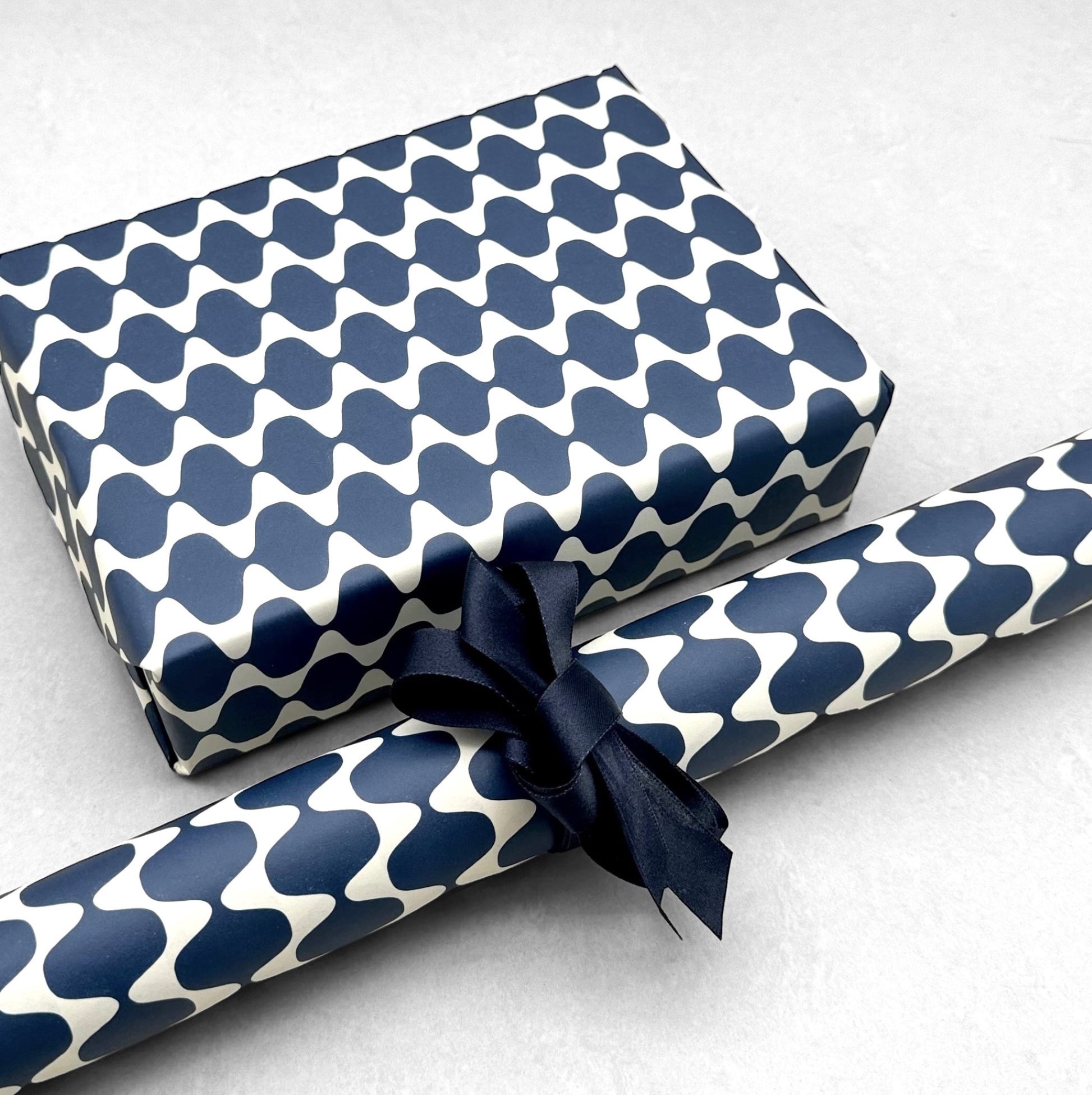 wrapping paper by Otto Editions with a cut-out wavy design in white on an indigo background. Pictured wrapped as a present with a roll of the paper