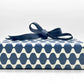wrapping paper by Otto Editions with a cut-out wavy design in white on an indigo background. Pictured wrapped as a present with a navy bow