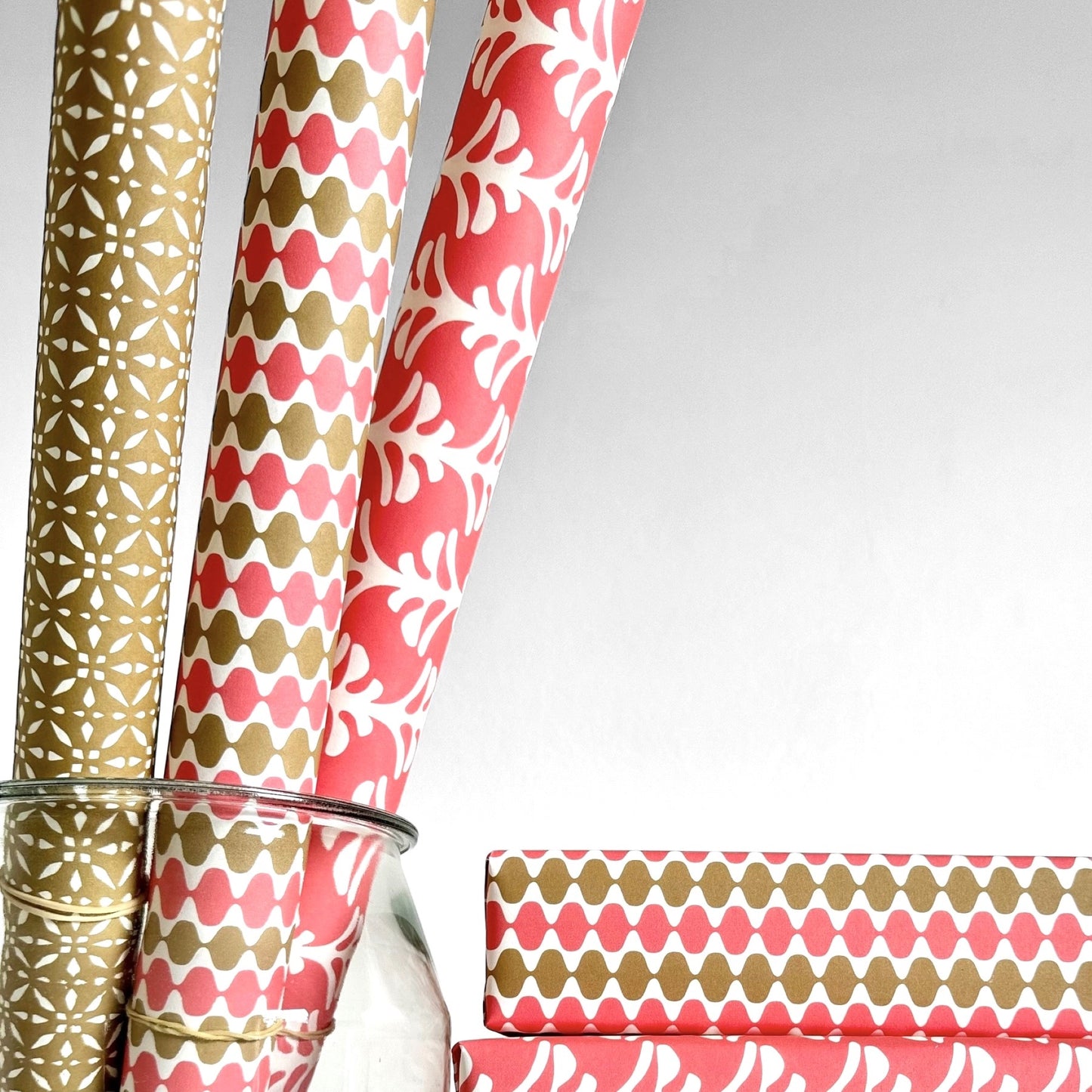 wrapping paper by Otto Editions with a cut-out wavy design in white on a coral and gold background. Pictured wrapped as a present with other designs