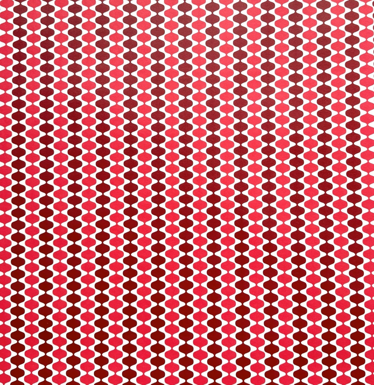 wrapping paper by Otto Editions with a cut-out wavy design in white on a pink and burgundy background. 