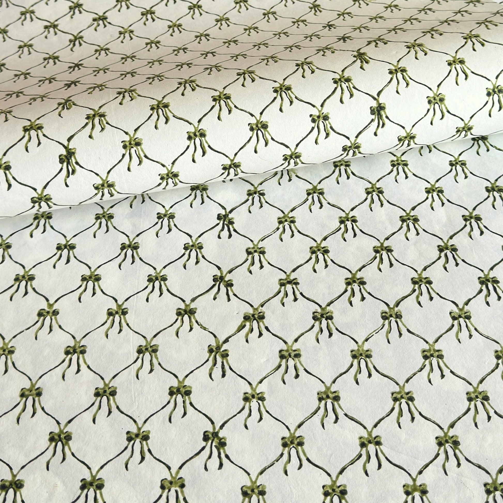 a sheet of hand block printed paper with a pattern of green bows on white