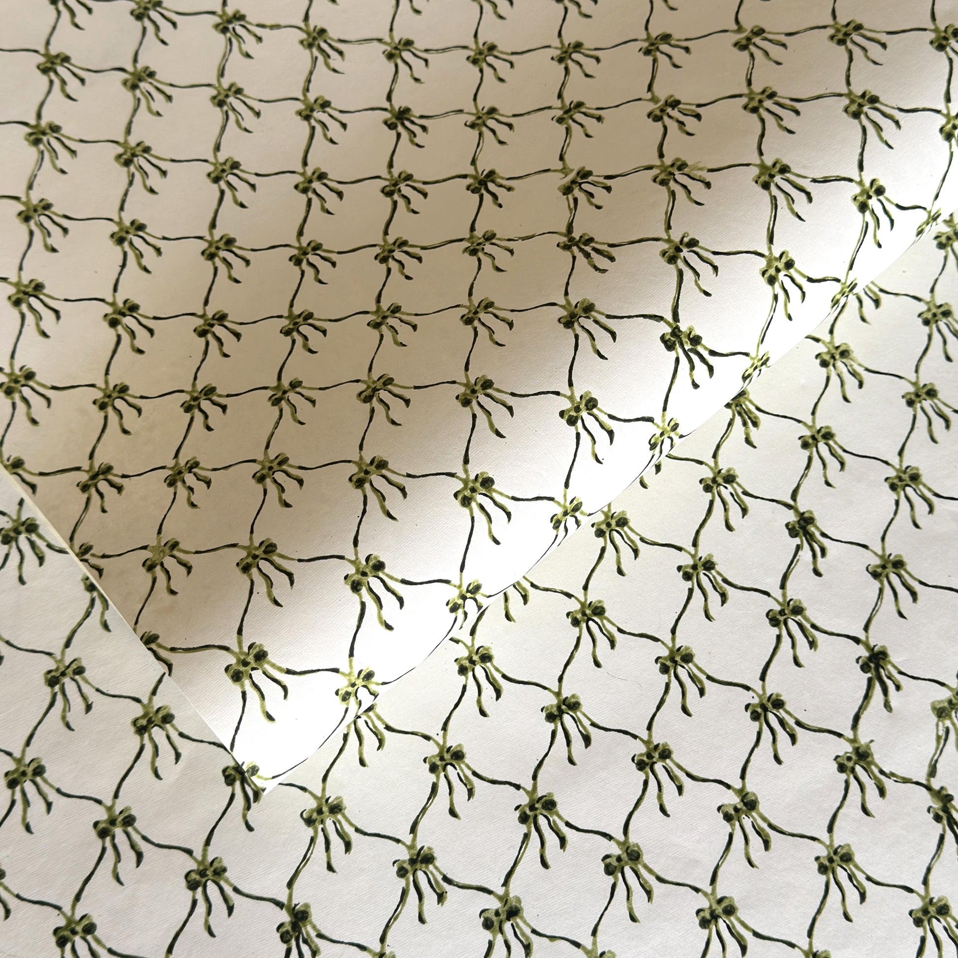 a sheet of hand block printed paper with a pattern of green bows on white
