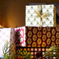 a sheet of hand block printed paper with a pattern of green bows on white. Pictured as a wrapped present with a ribbon at the top of a pile of presents