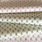 a sheet of hand block printed paper with a pattern of green bows on white, pictured alongside a version in red