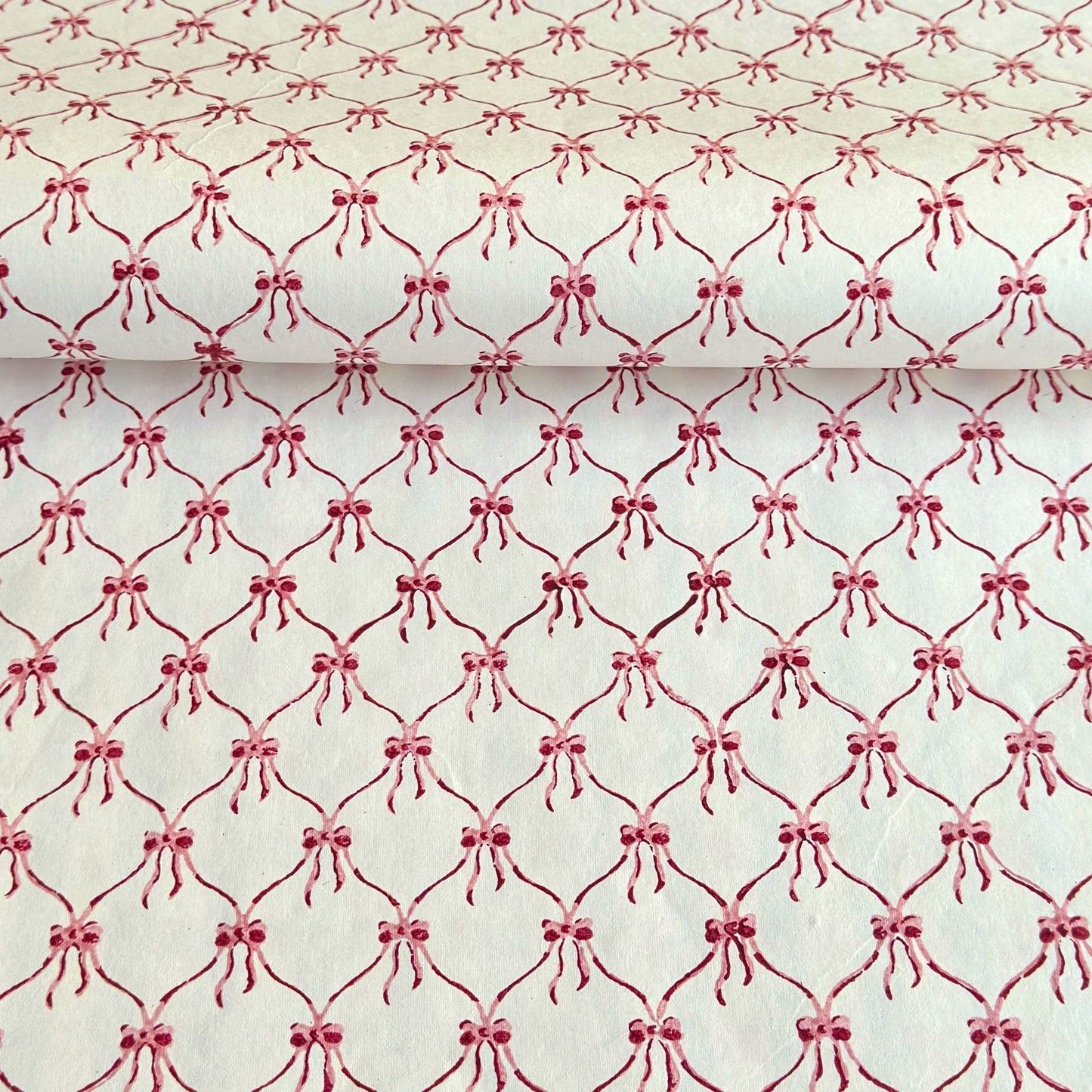 a sheet of hand block printed paper with a red and pink bow design on white