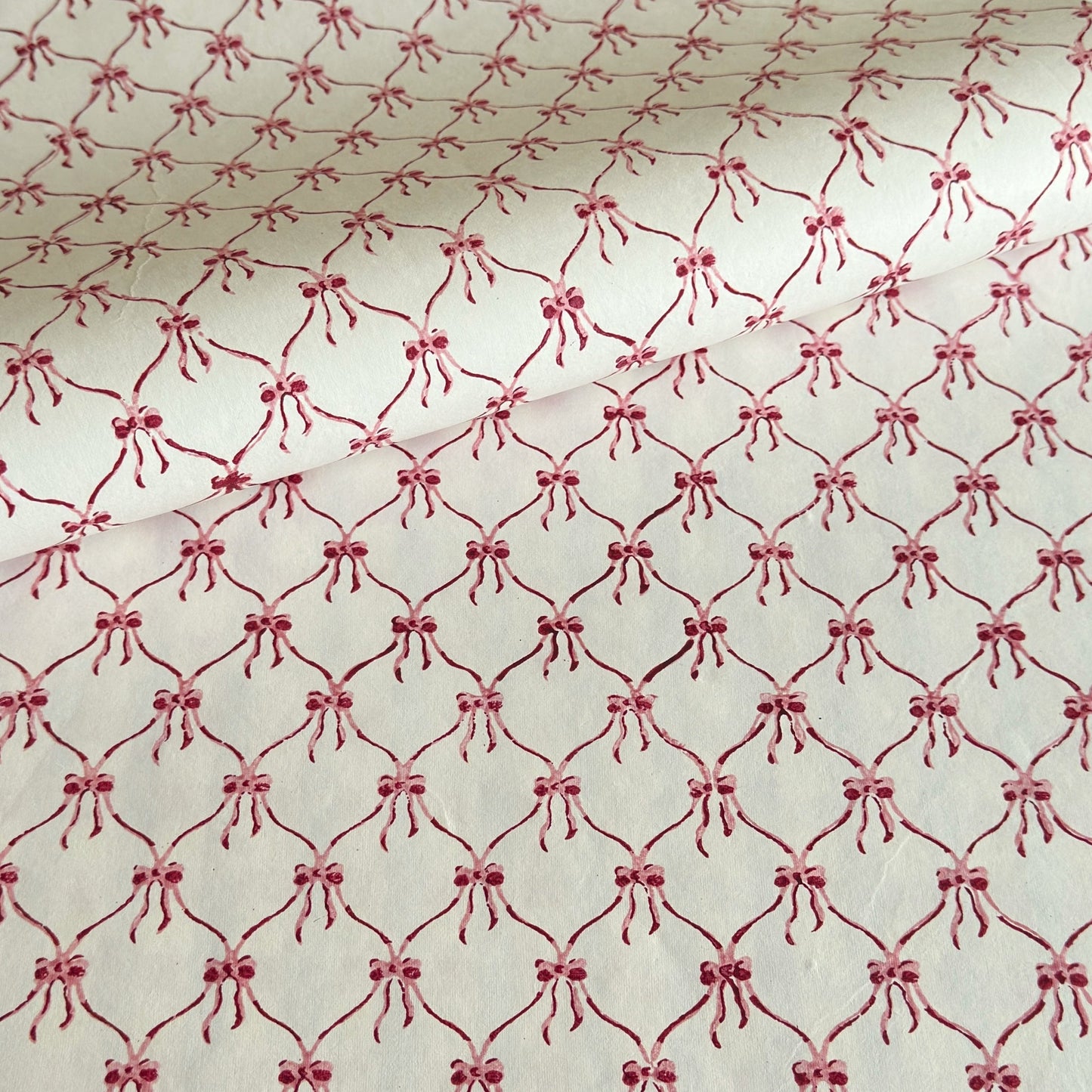 a sheet of hand block printed paper with a red and pink bow design on white