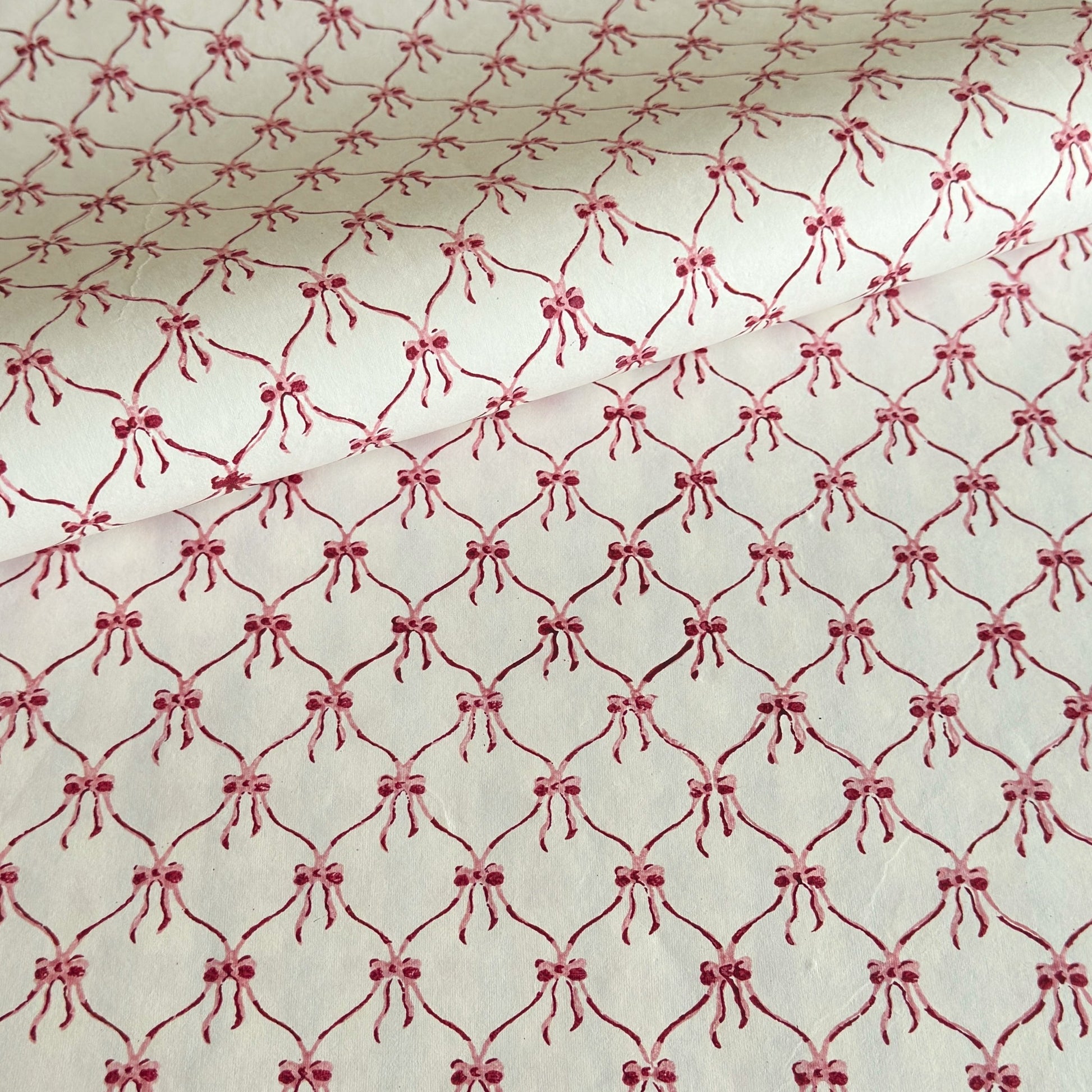 a sheet of hand block printed paper with a red and pink bow design on white
