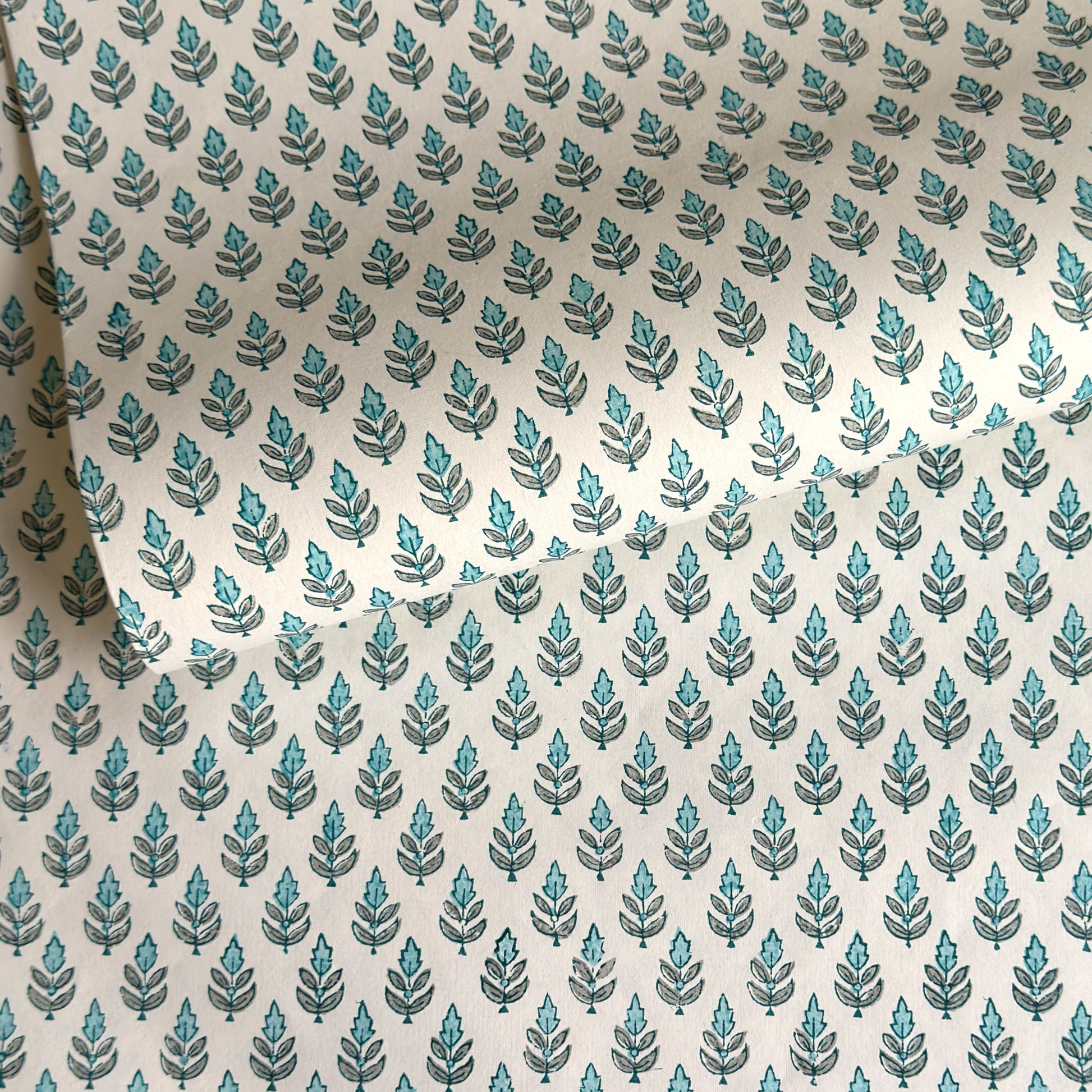 hand block printed wrapping paper by paper mirchi with a repeat floral pattern in turquoise and soft green on white backdrop