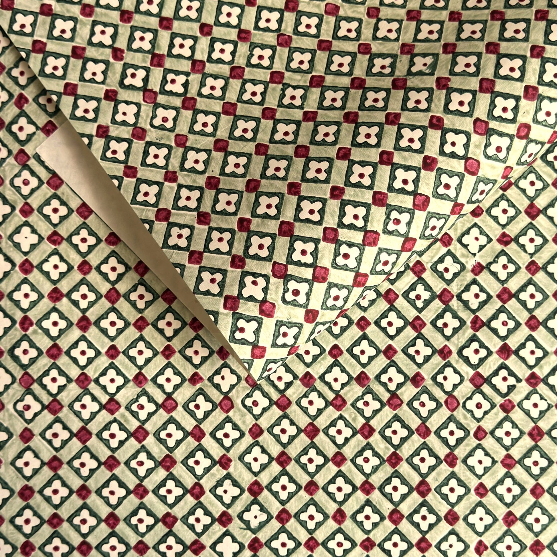 Hand block printed wrapping paper with a floral checked pattern in sage green and red.