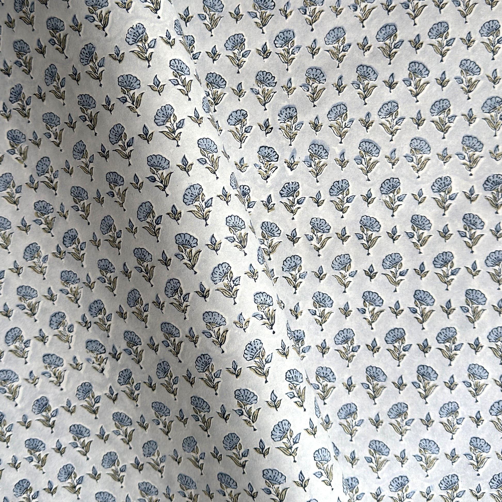 a hand block printed sheet of wrapping paper with a ditsy floral print in soft blue