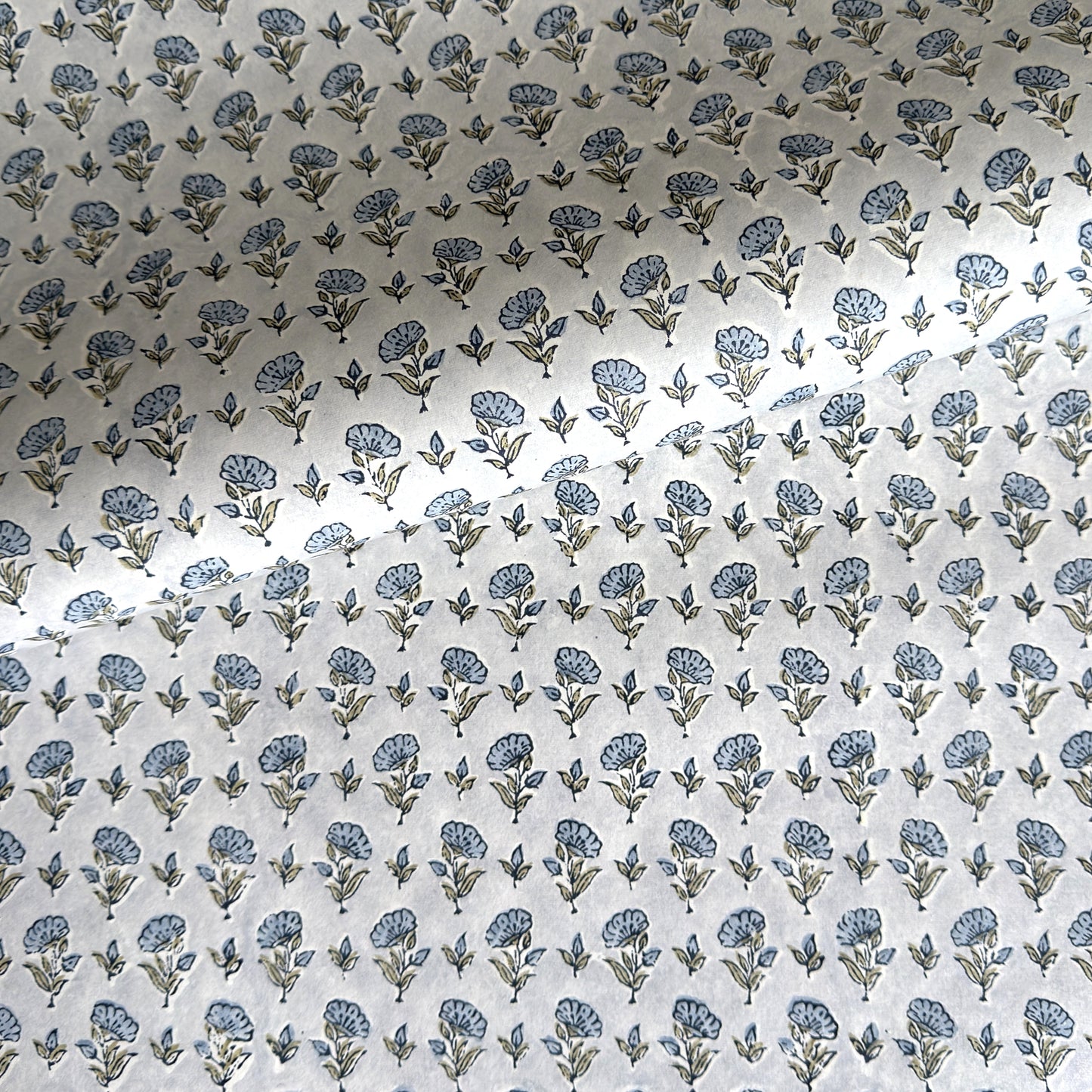 a hand block printed sheet of wrapping paper with a ditsy floral print in soft blue