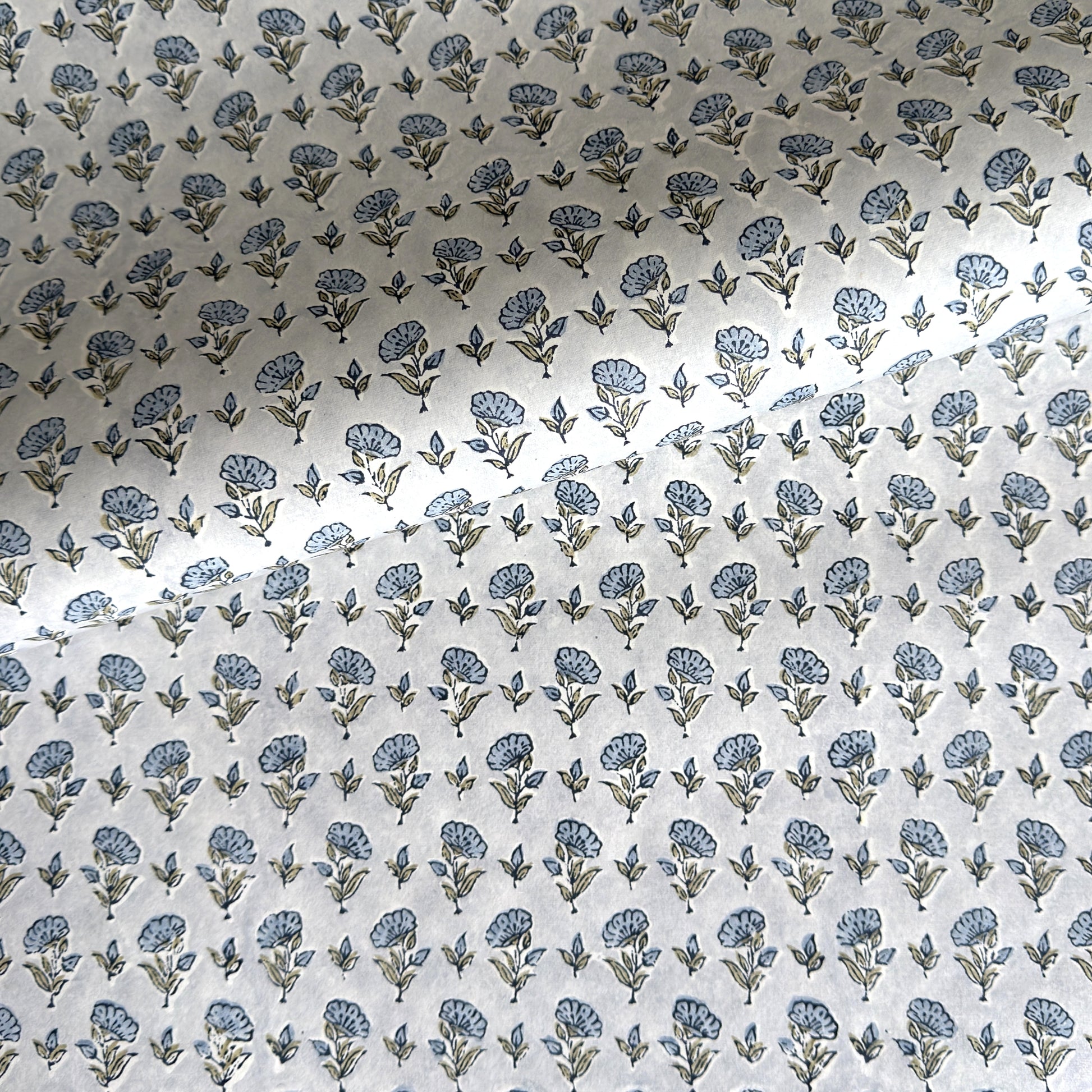 a hand block printed sheet of wrapping paper with a ditsy floral print in soft blue