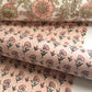 a hand block printed sheet of wrapping paper with a ditsy floral print in pink. Pictured rolled with another design