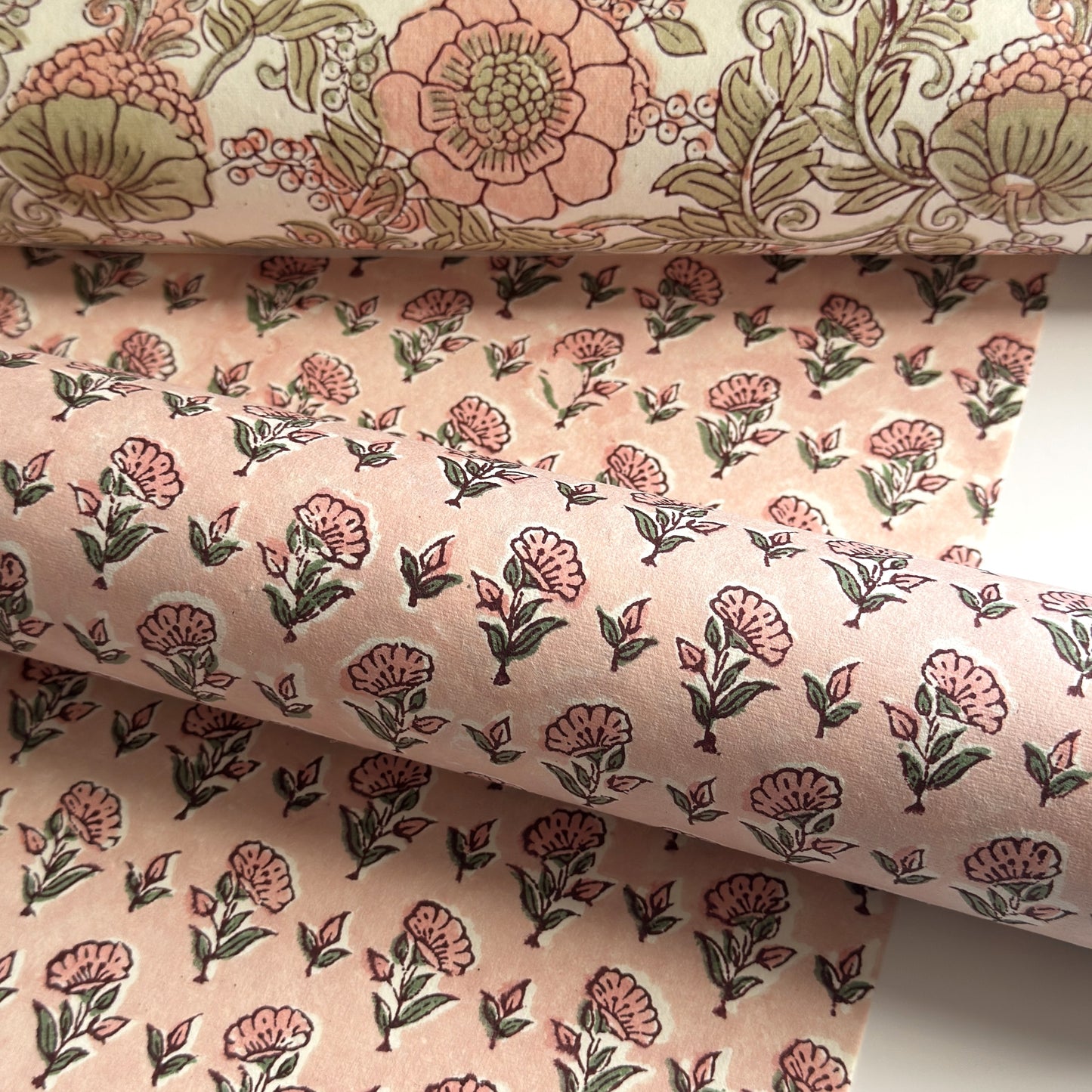 a hand block printed sheet of wrapping paper with a ditsy floral print in pink. Pictured rolled with another design