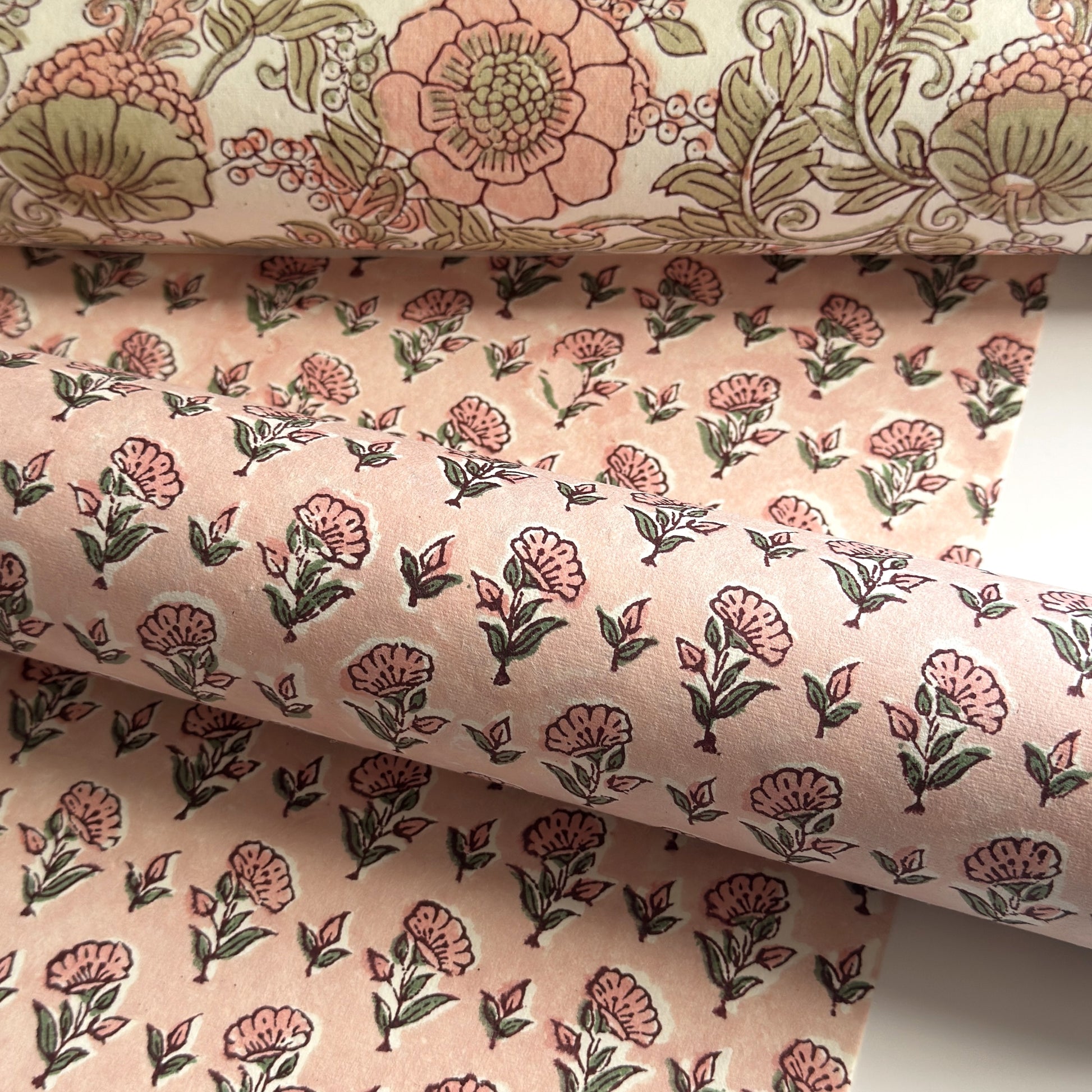 a hand block printed sheet of wrapping paper with a ditsy floral print in pink. Pictured rolled with another design