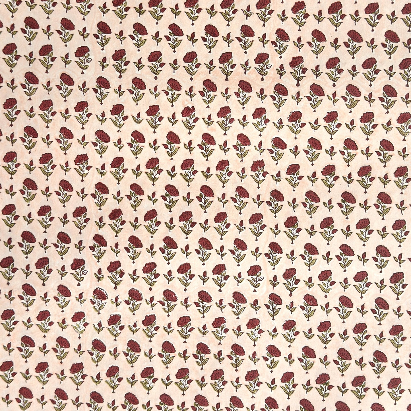 a sheet of hand block printed paper with a ditsy floral design in red and green on pink background
