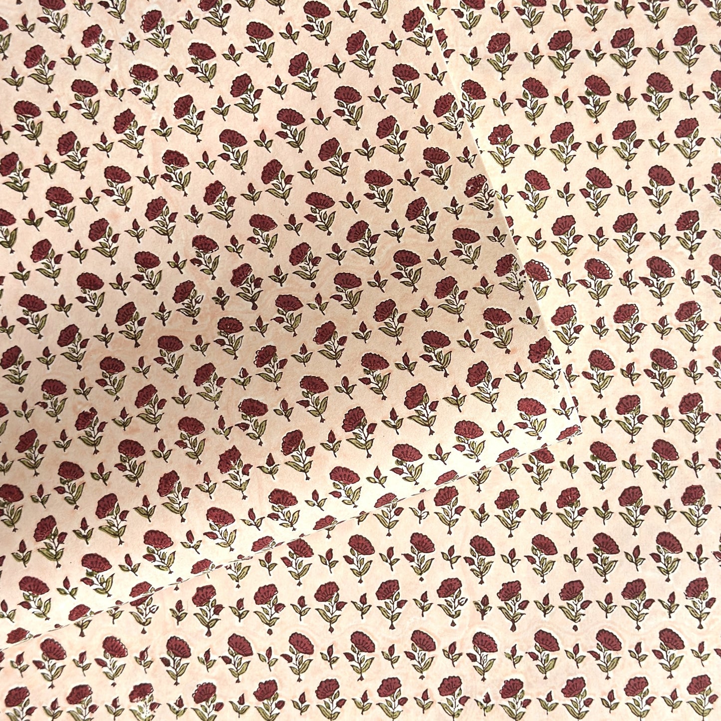 a sheet of hand block printed paper with a ditsy floral design in red and green on pink background