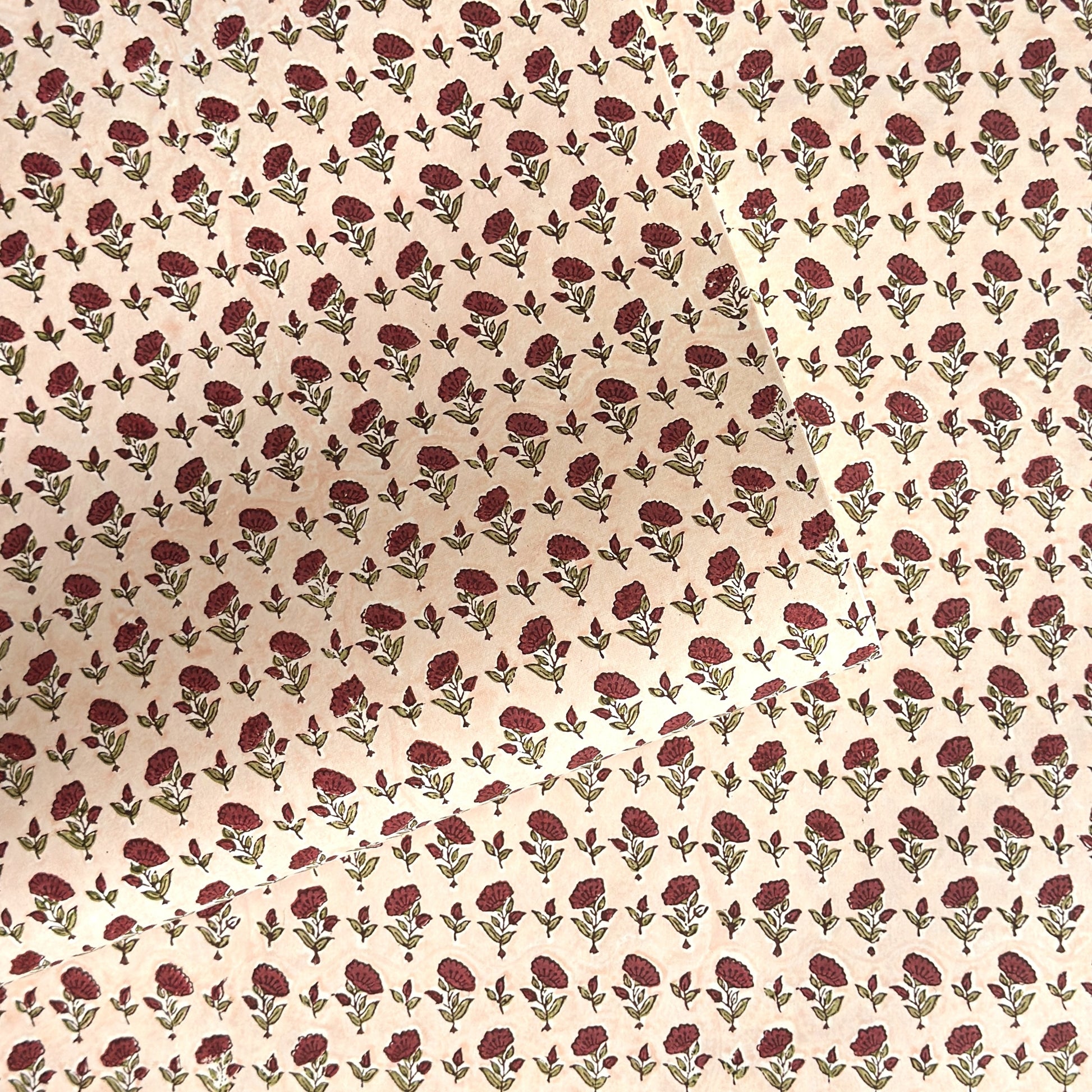 a sheet of hand block printed paper with a ditsy floral design in red and green on pink background