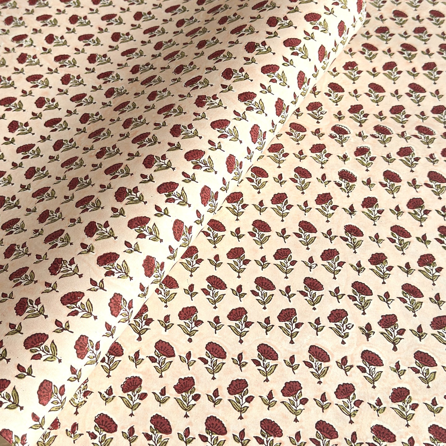 a sheet of hand block printed paper with a ditsy floral design in red and green on pink background