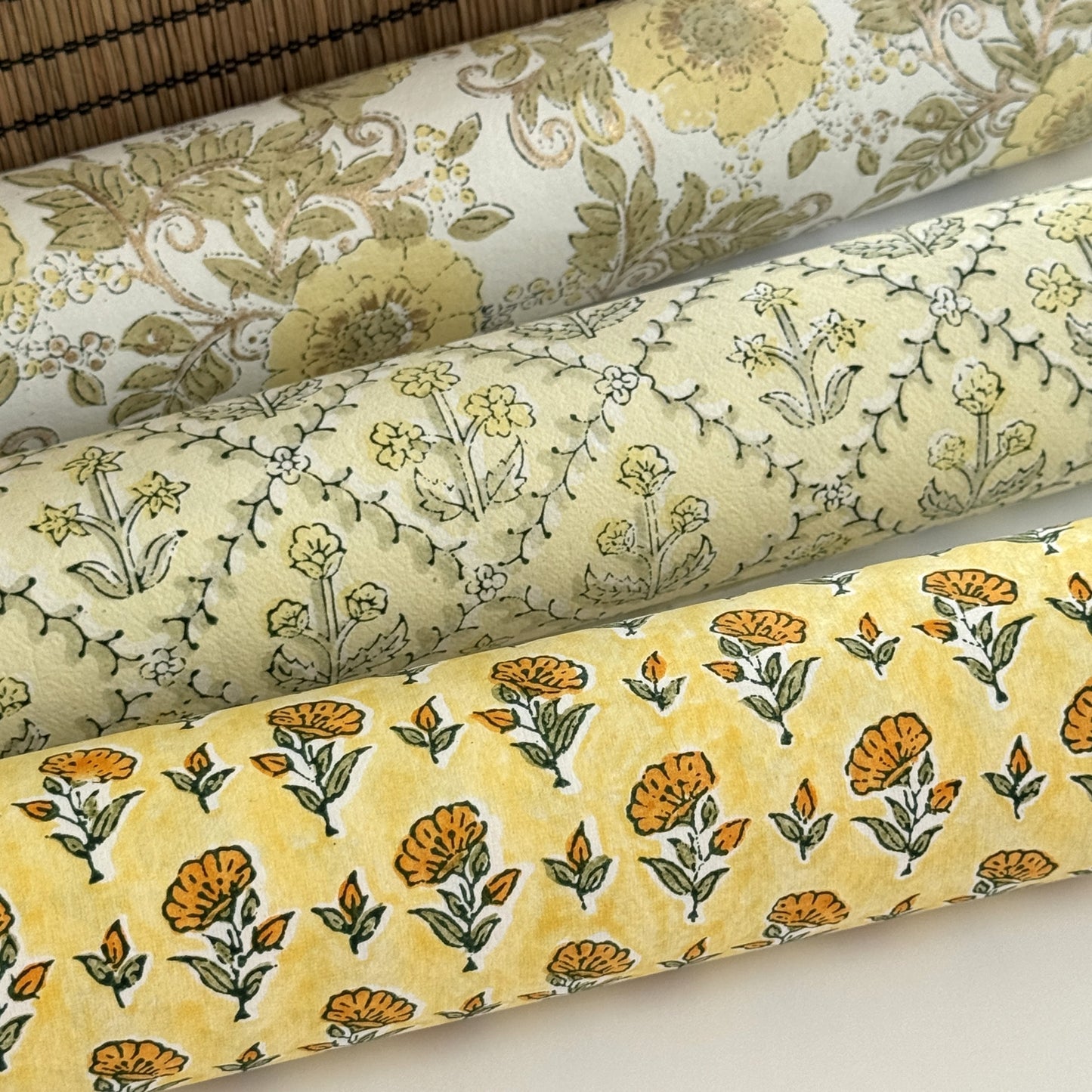 a sheet of hand block printed wrapping paper with a ditsy floral flower design in yellow. Pictured rolled with other designs.