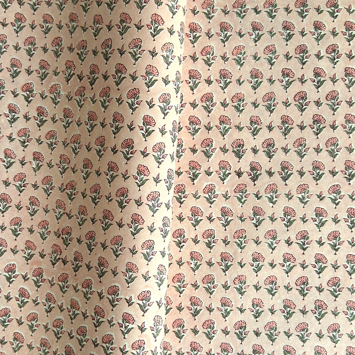 a hand block printed sheet of wrapping paper with a ditsy floral print in pink. Pictured rolled with another design