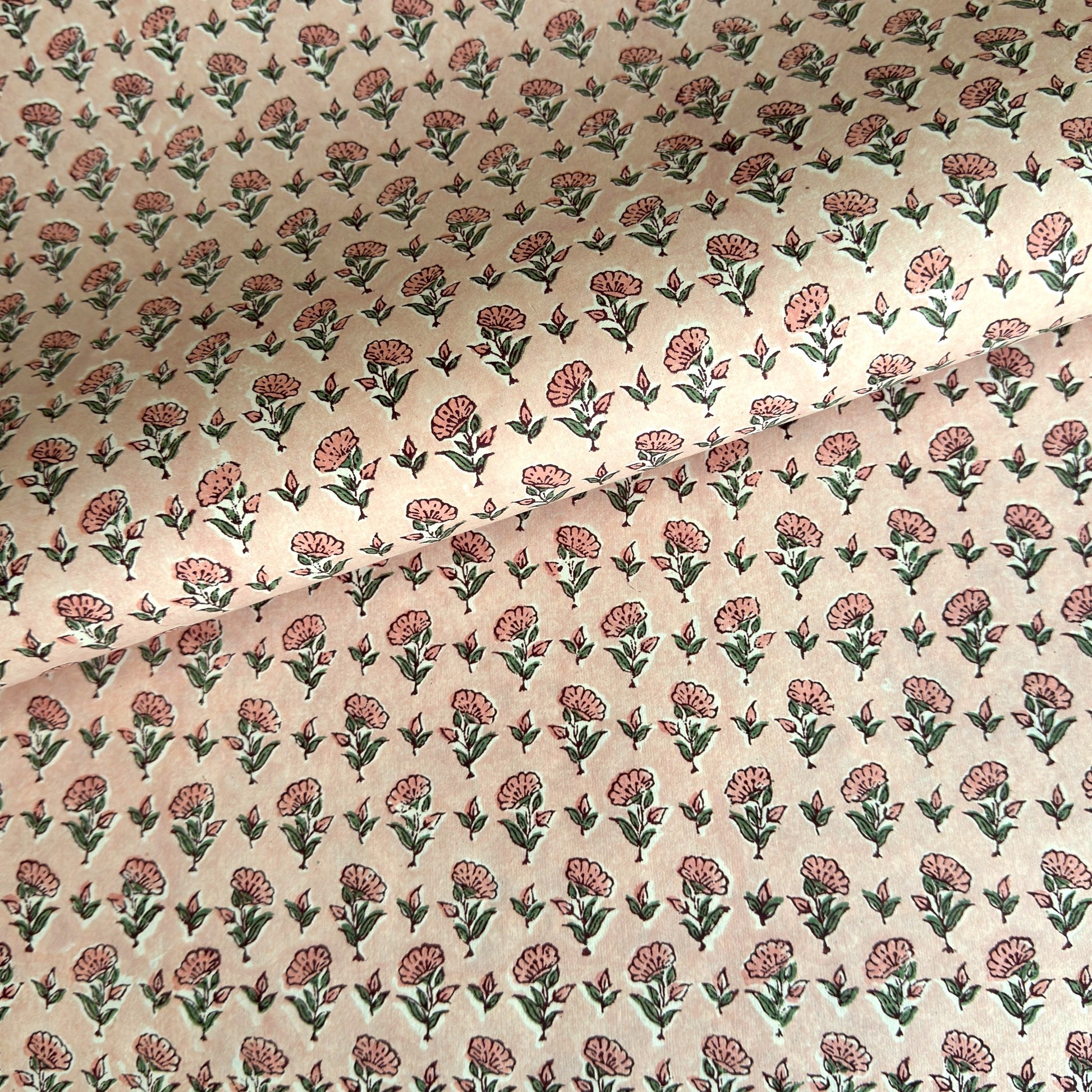 a hand block printed sheet of wrapping paper with a ditsy floral print in pink. Pictured rolled with another design