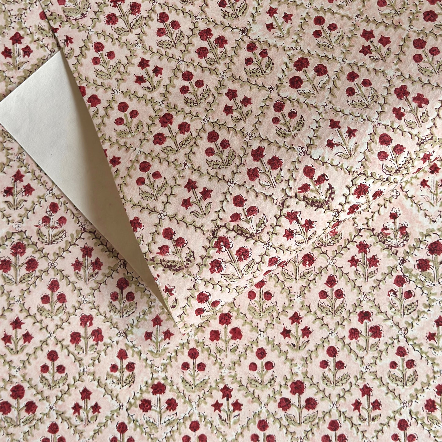 a sheet of hand block printed paper with a floral trellis design in blush pink, sage green and deep red