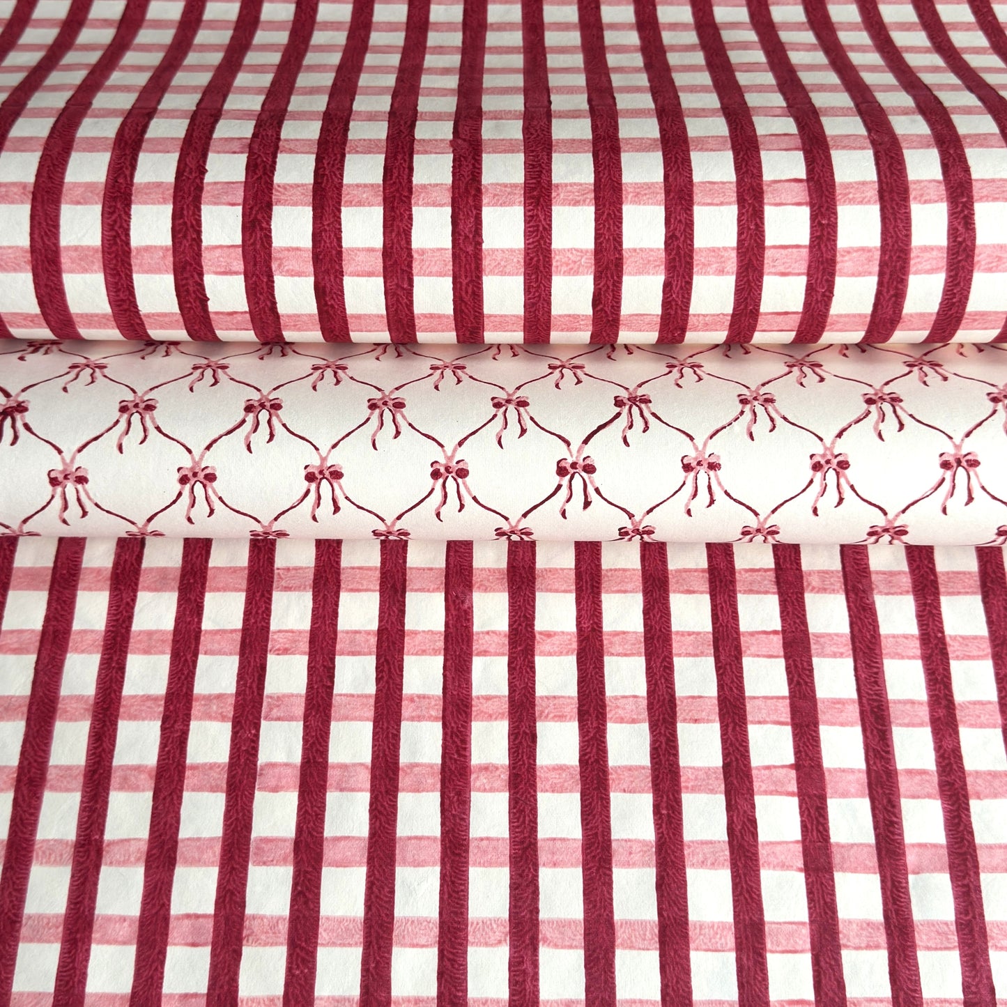 red and pink gingham pattern hand block printed on a white sheet of cotton paper. Pictured with another paper that has pink bows