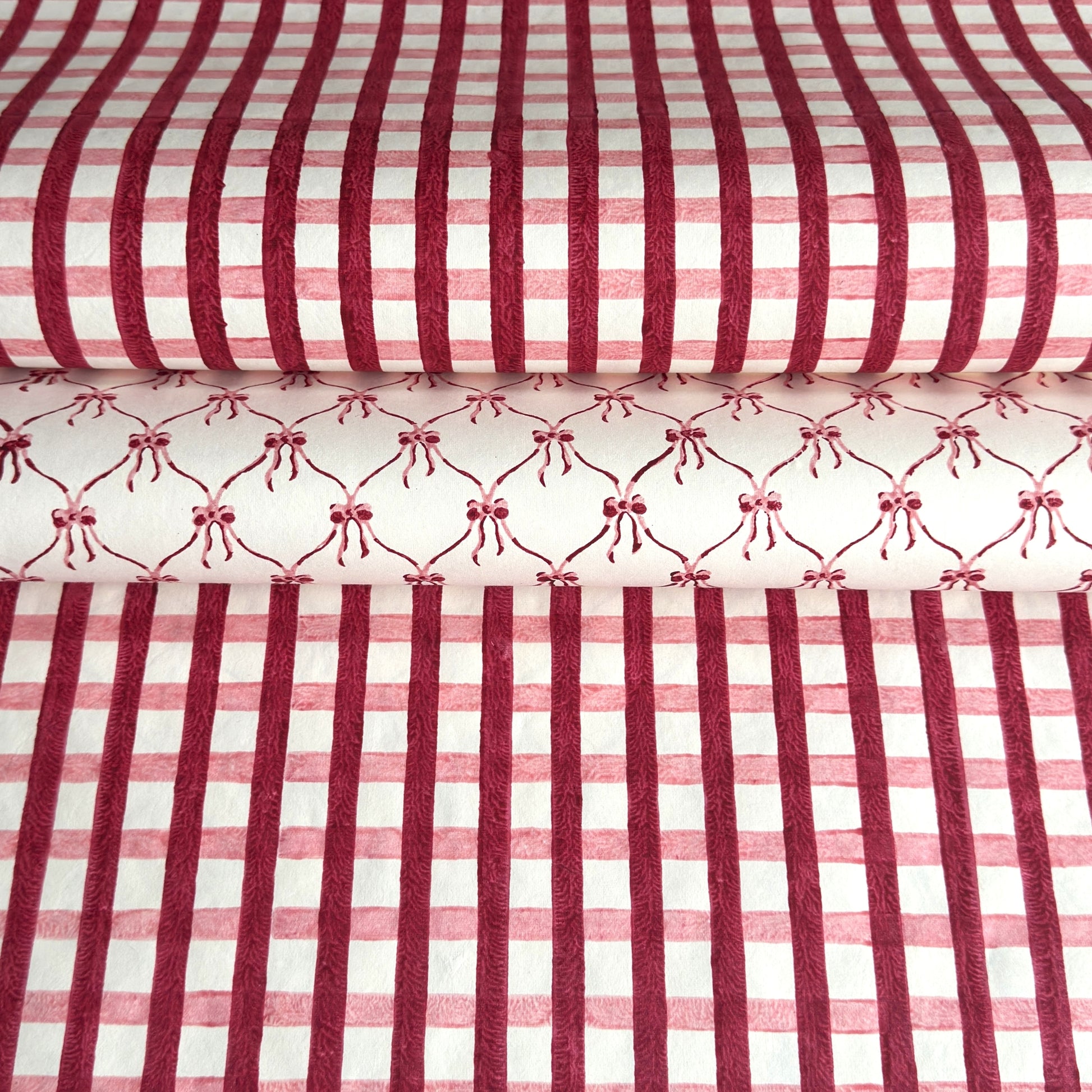 red and pink gingham pattern hand block printed on a white sheet of cotton paper. Pictured with another paper that has pink bows