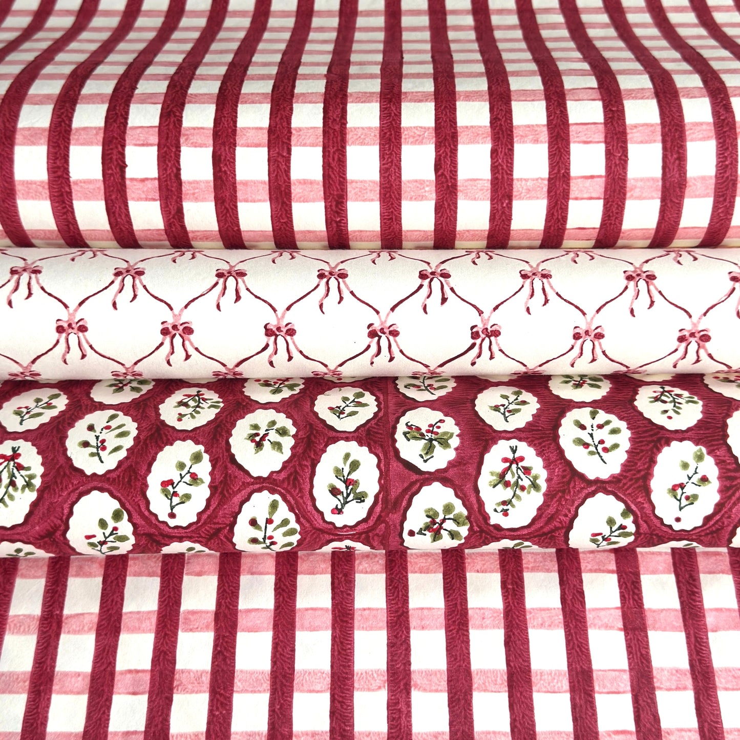 red and pink gingham pattern hand block printed on a white sheet of cotton paper, Picture with two other paper designs, one with pink bows on white and another with winter foliage in red