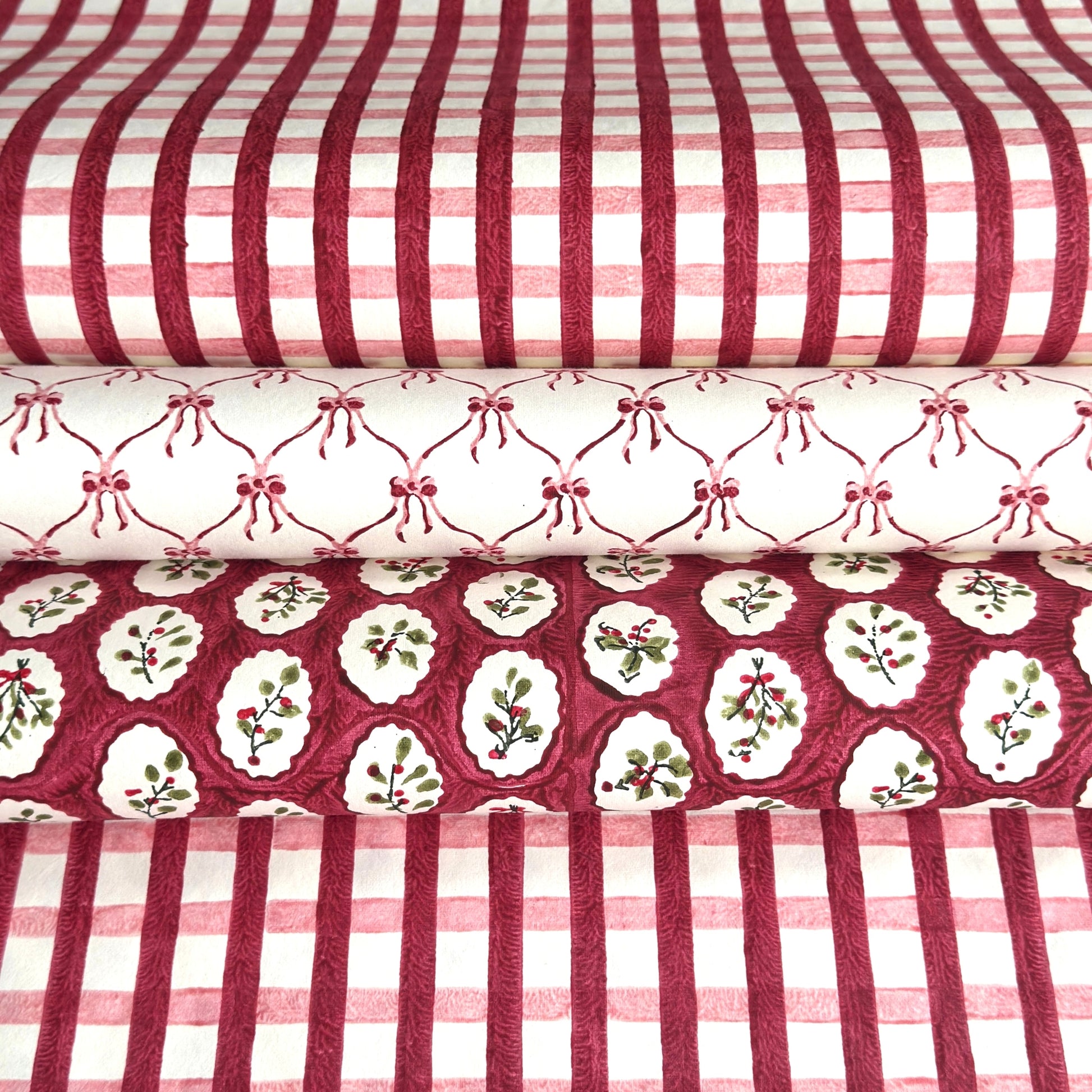 red and pink gingham pattern hand block printed on a white sheet of cotton paper, Picture with two other paper designs, one with pink bows on white and another with winter foliage in red