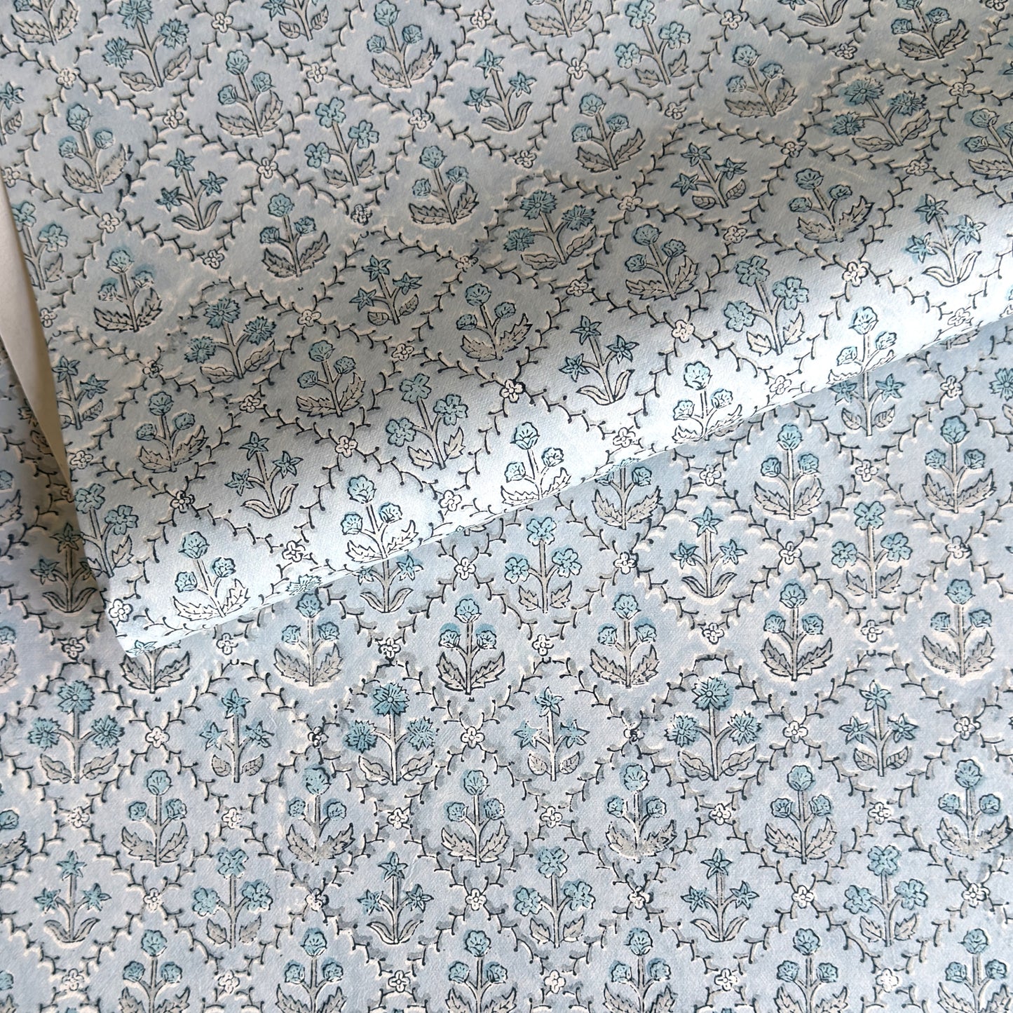 a sheet of hand block printed wrapping paper with a floral lattice design in soft blue