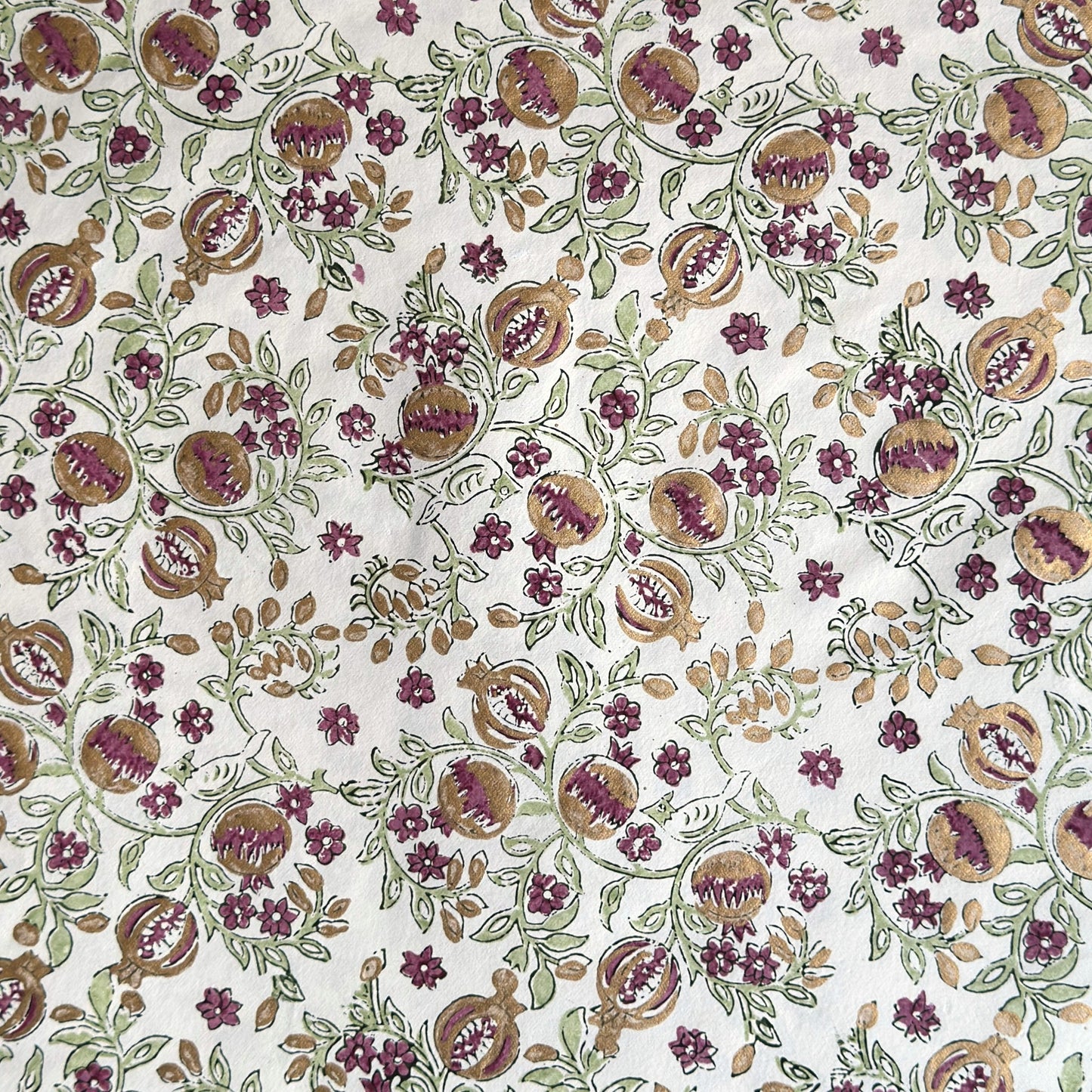 Hand block printed wrapping paper with a pattern of pomegranates in cherry red, green and gold.