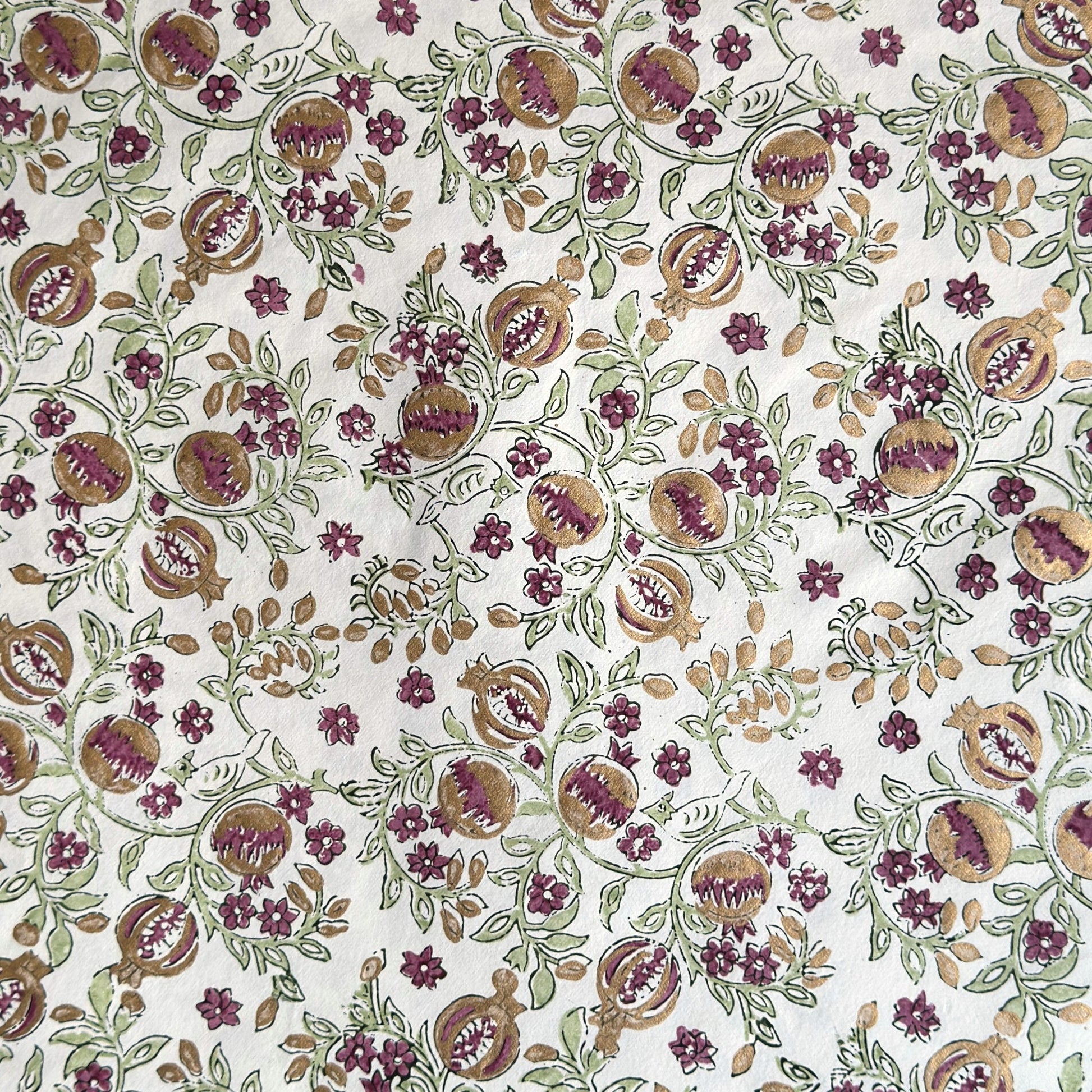 Hand block printed wrapping paper with a pattern of pomegranates in cherry red, green and gold.