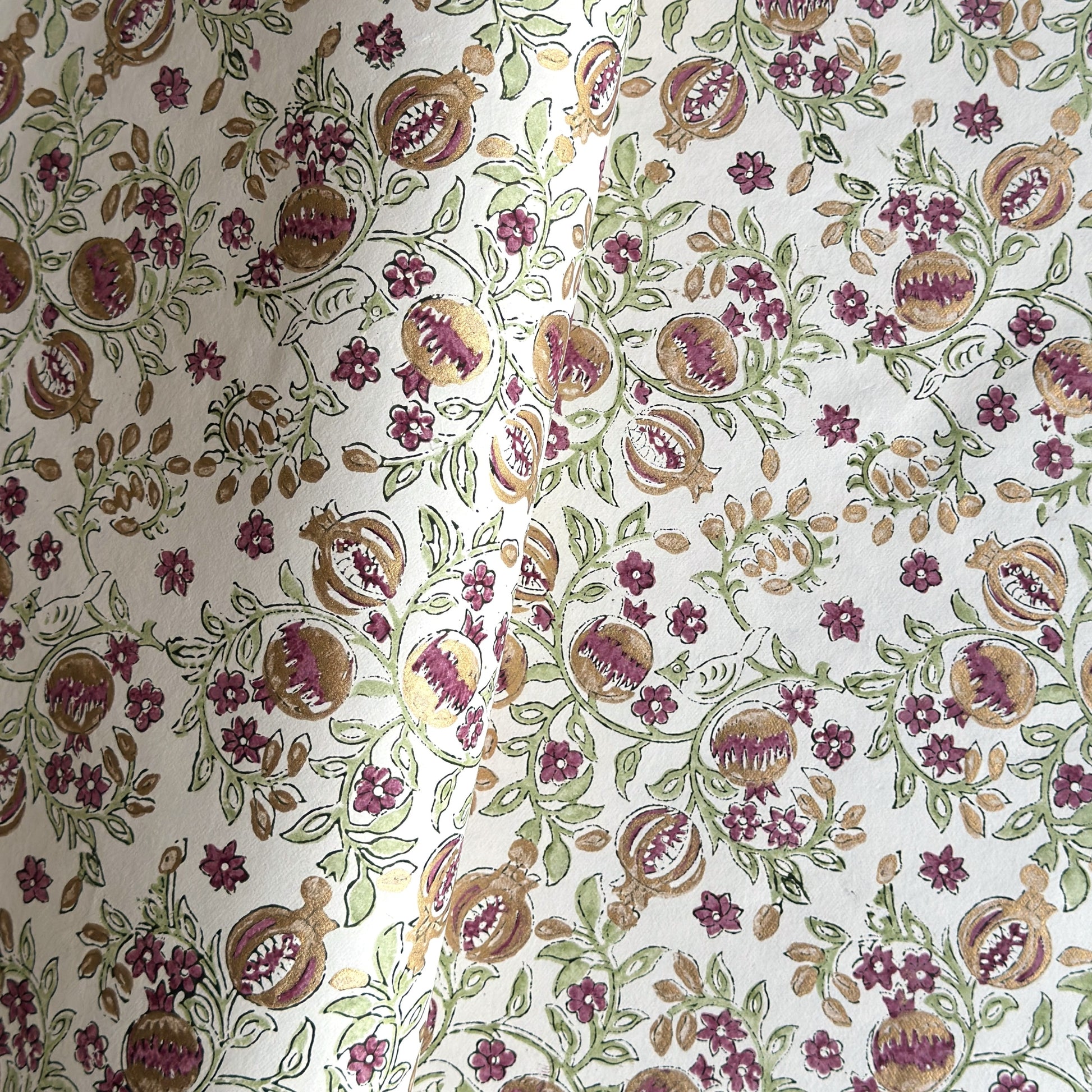 Hand block printed wrapping paper with a pattern of pomegranates in cherry red, green and gold.