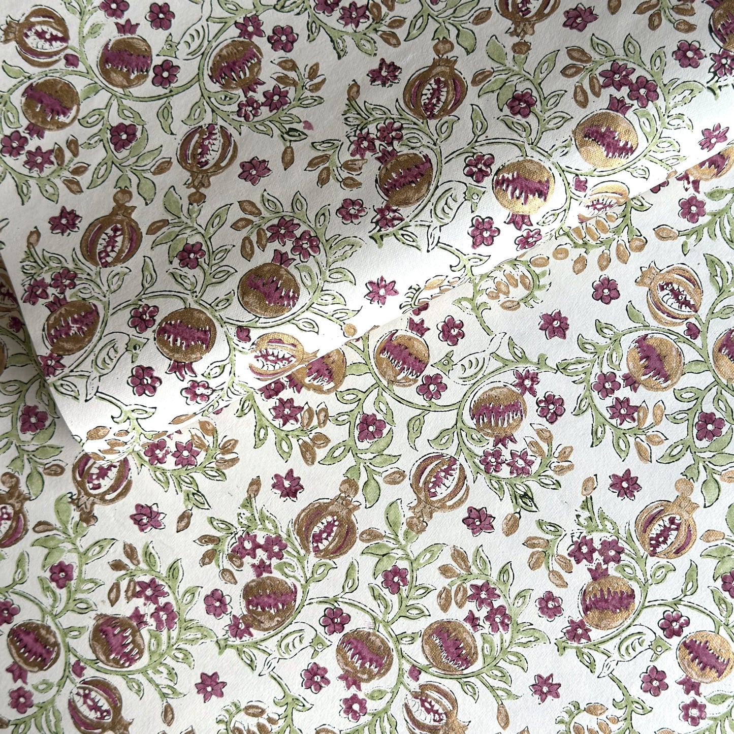 Hand block printed wrapping paper with a pattern of pomegranates in cherry red, green and gold.