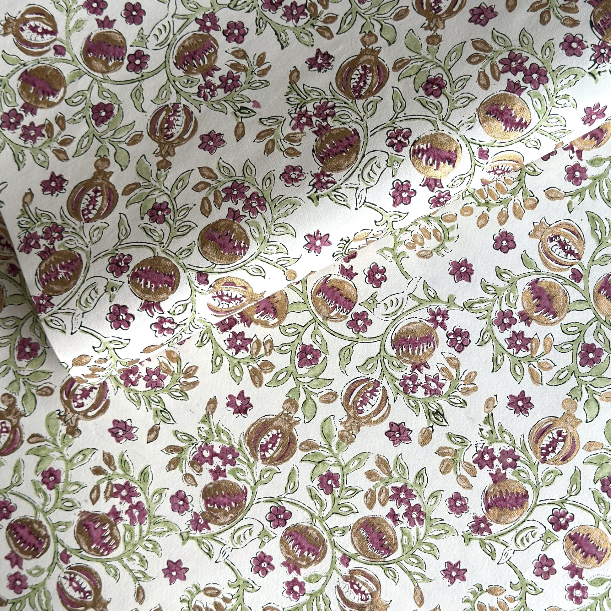 Hand block printed wrapping paper with a pattern of pomegranates in cherry red, green and gold.