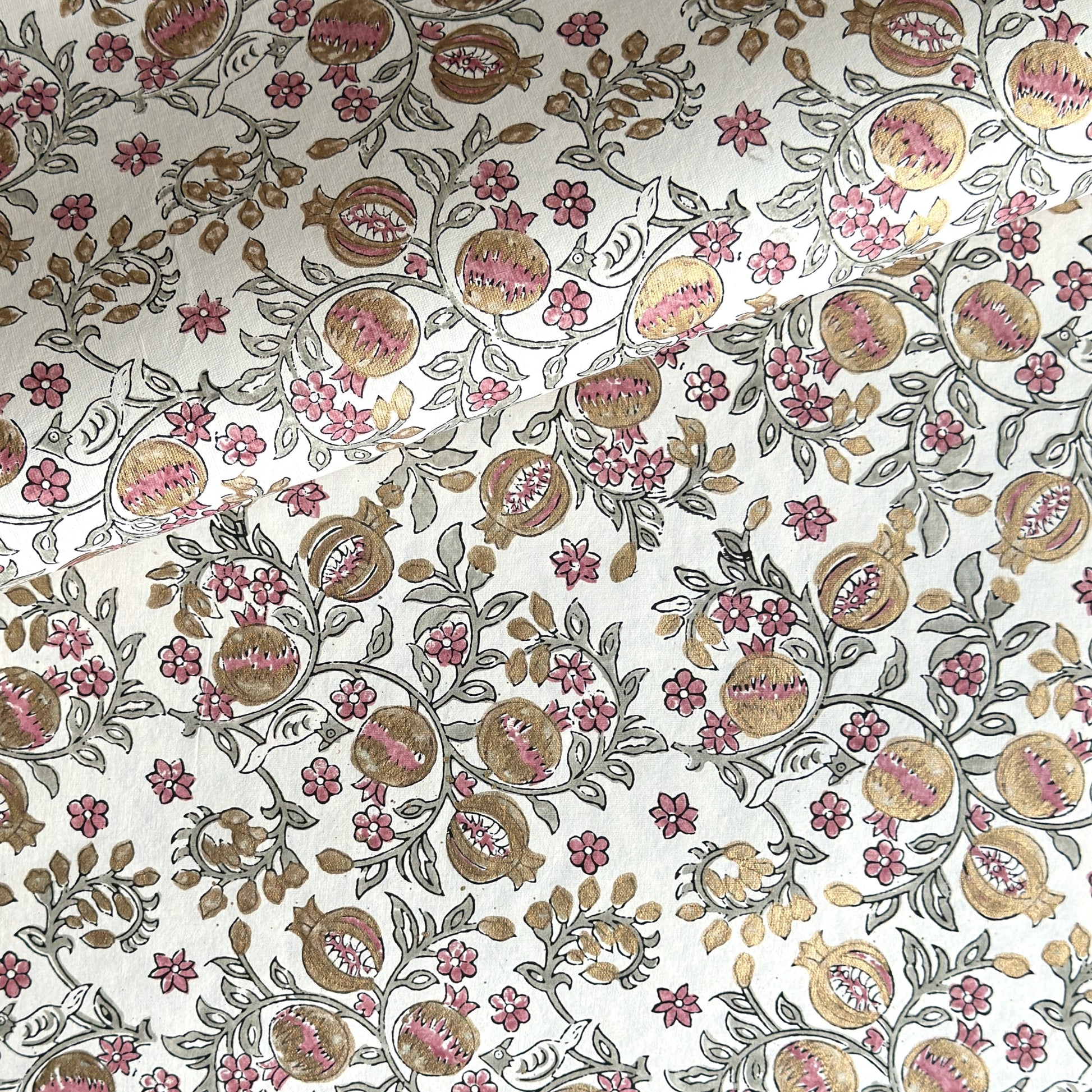 hand block printed wrapping paper by Paper Mirchi.  Repeat pattern of pomegranates in pink and green within a gold accent design.