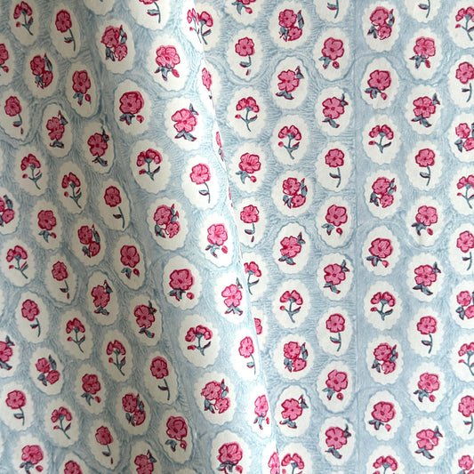 a sheet of hand block printed wrapping paper with a ditsy floral pattern of pink flowers in white ovals with a soft blue backdrop