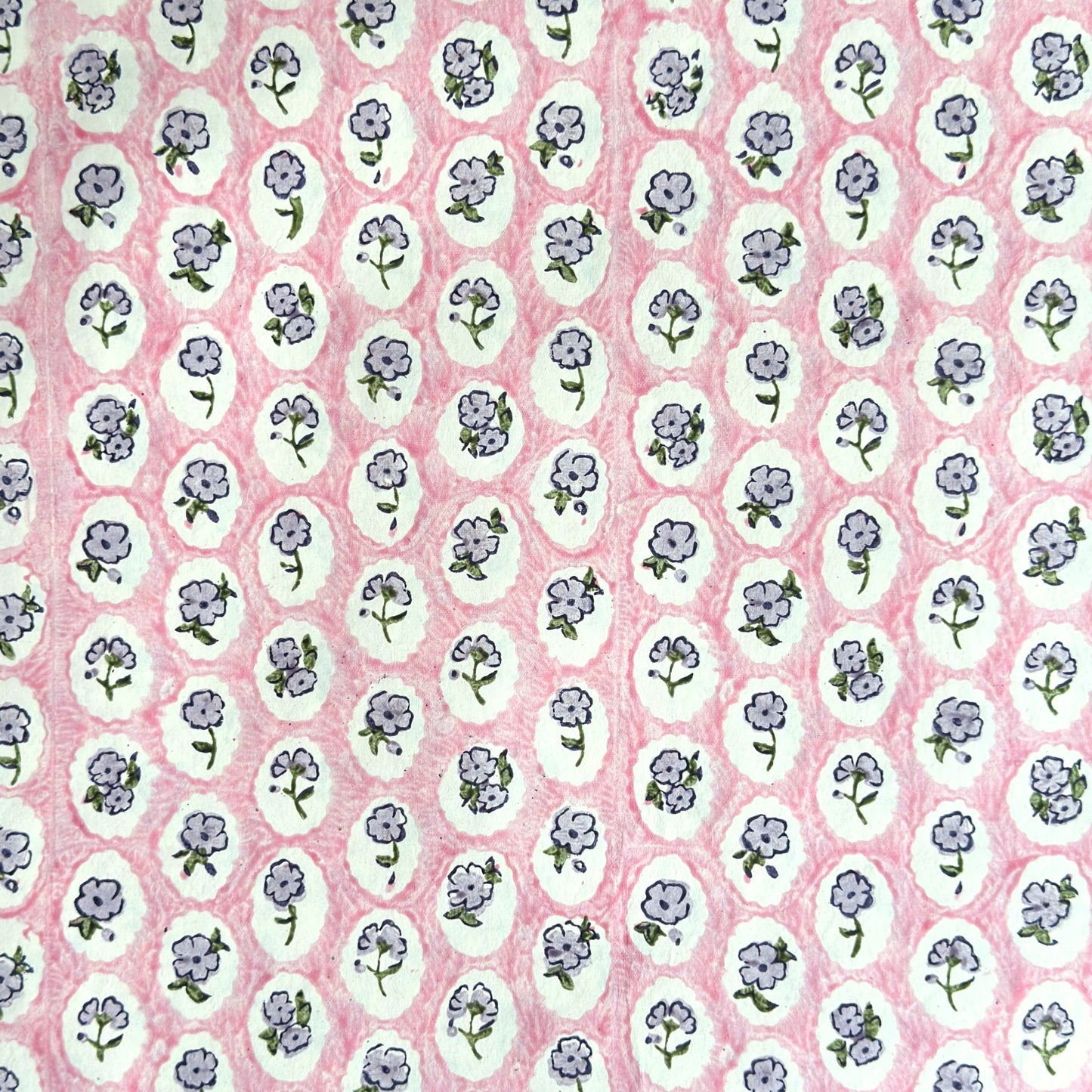 a sheet of hand block printed paper with a ditsy floral design, little violet flowers in a white oval with a pink background