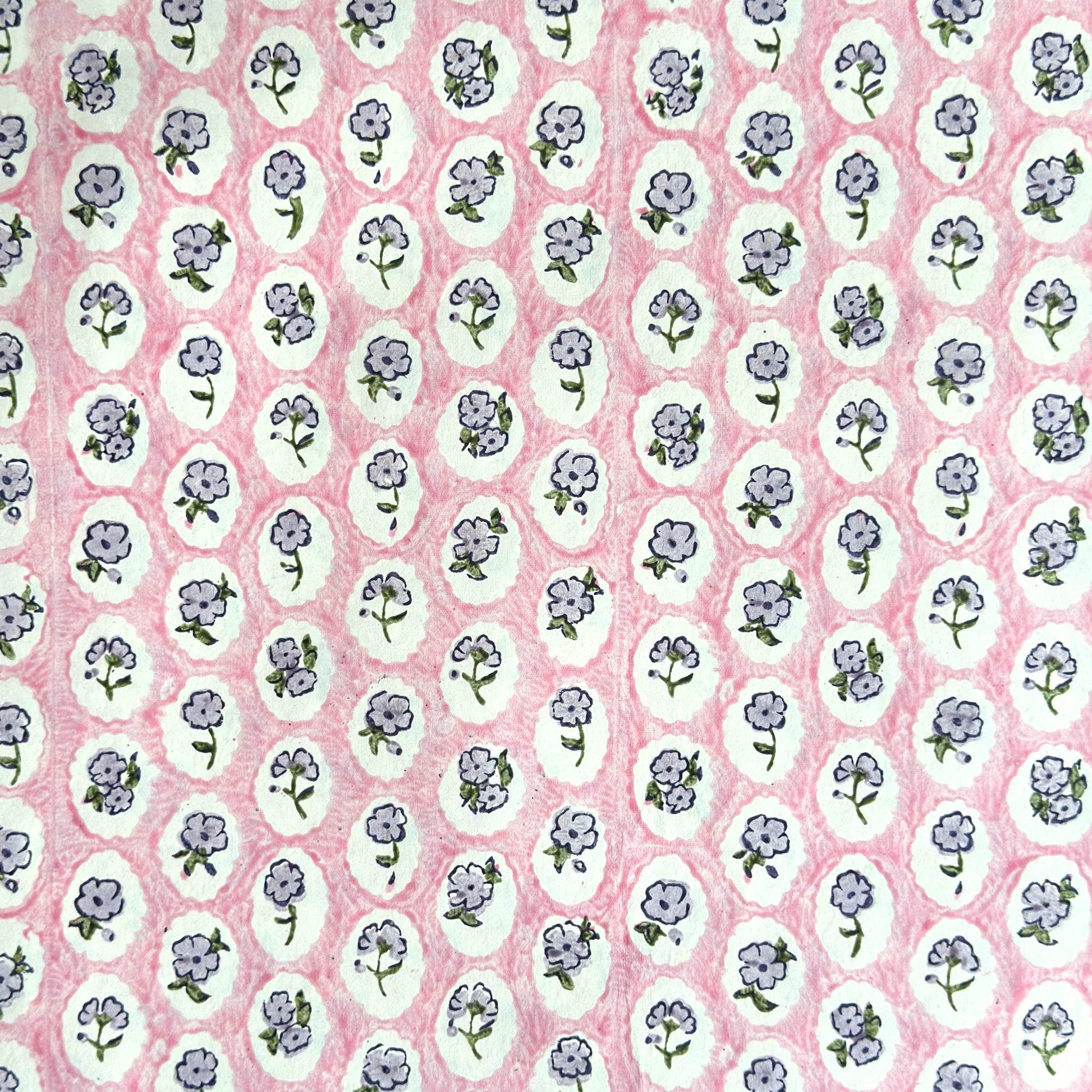 a sheet of hand block printed paper with a ditsy floral design, little violet flowers in a white oval with a pink background