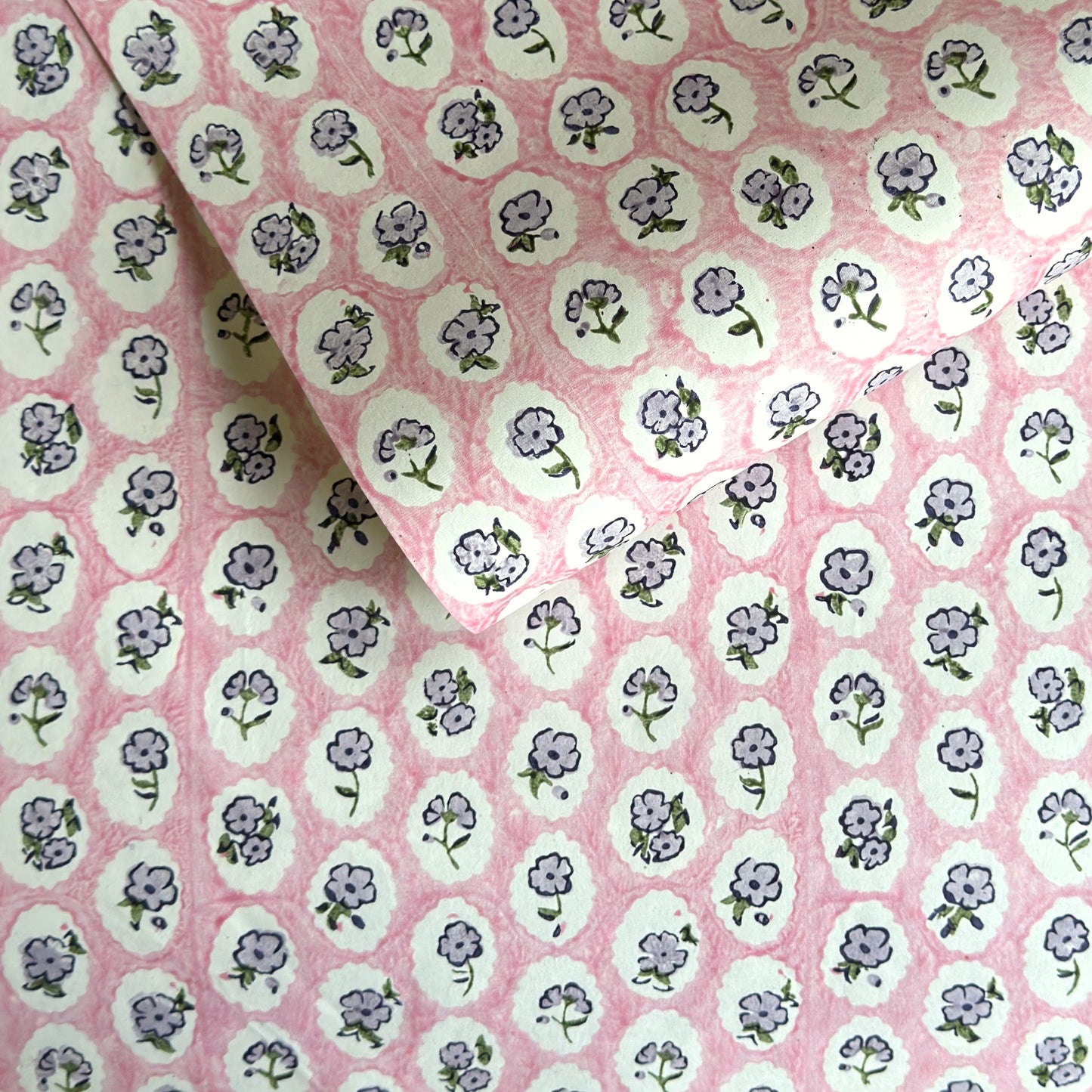 a sheet of hand block printed paper with a ditsy floral design, little violet flowers in a white oval with a pink background