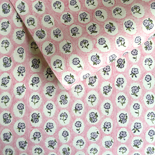 a sheet of hand block printed paper with a ditsy floral design, little violet flowers in a white oval with a pink background