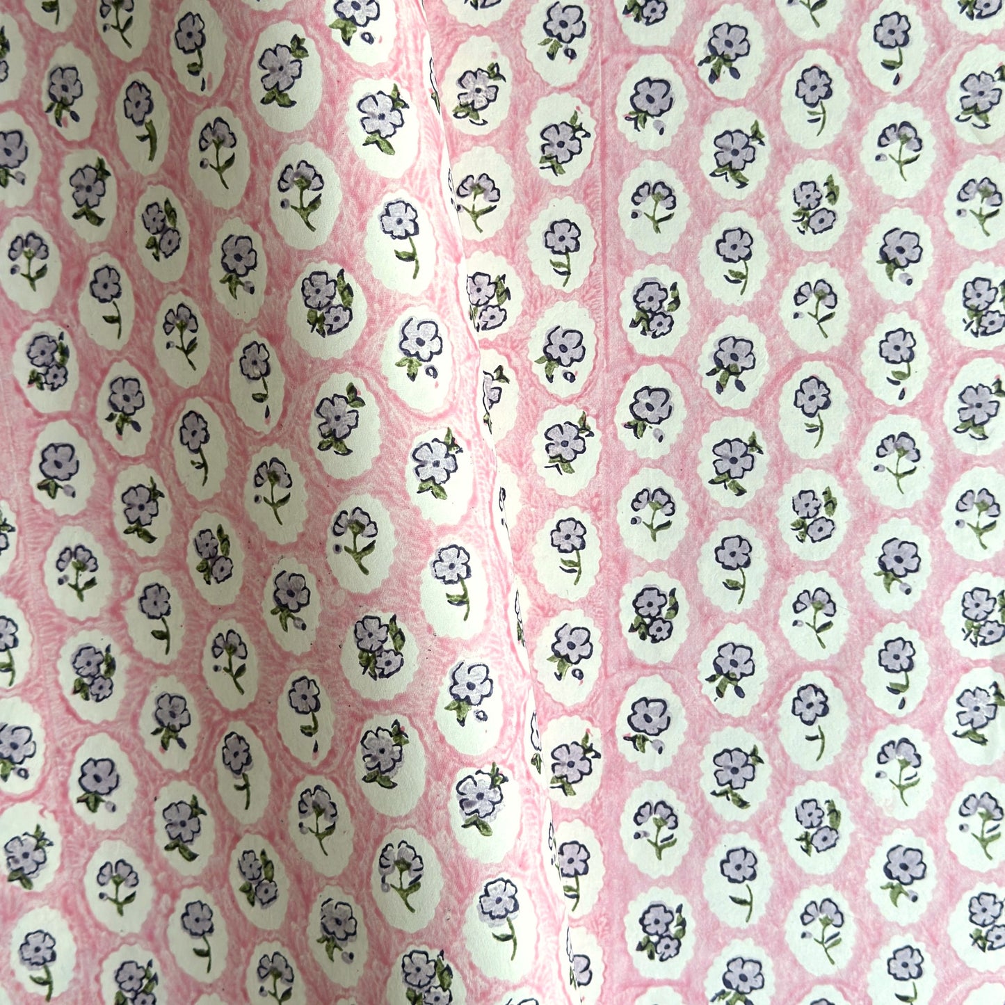 a sheet of hand block printed paper with a ditsy floral design, little violet flowers in a white oval with a pink background