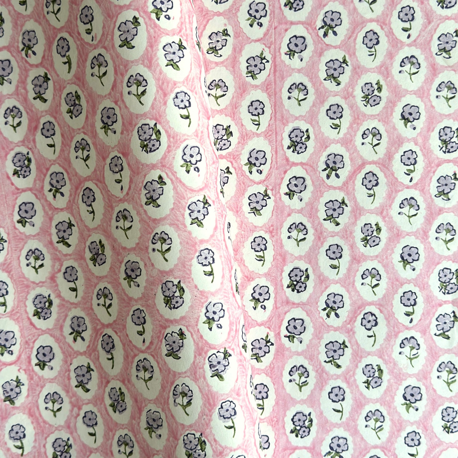 a sheet of hand block printed paper with a ditsy floral design, little violet flowers in a white oval with a pink background