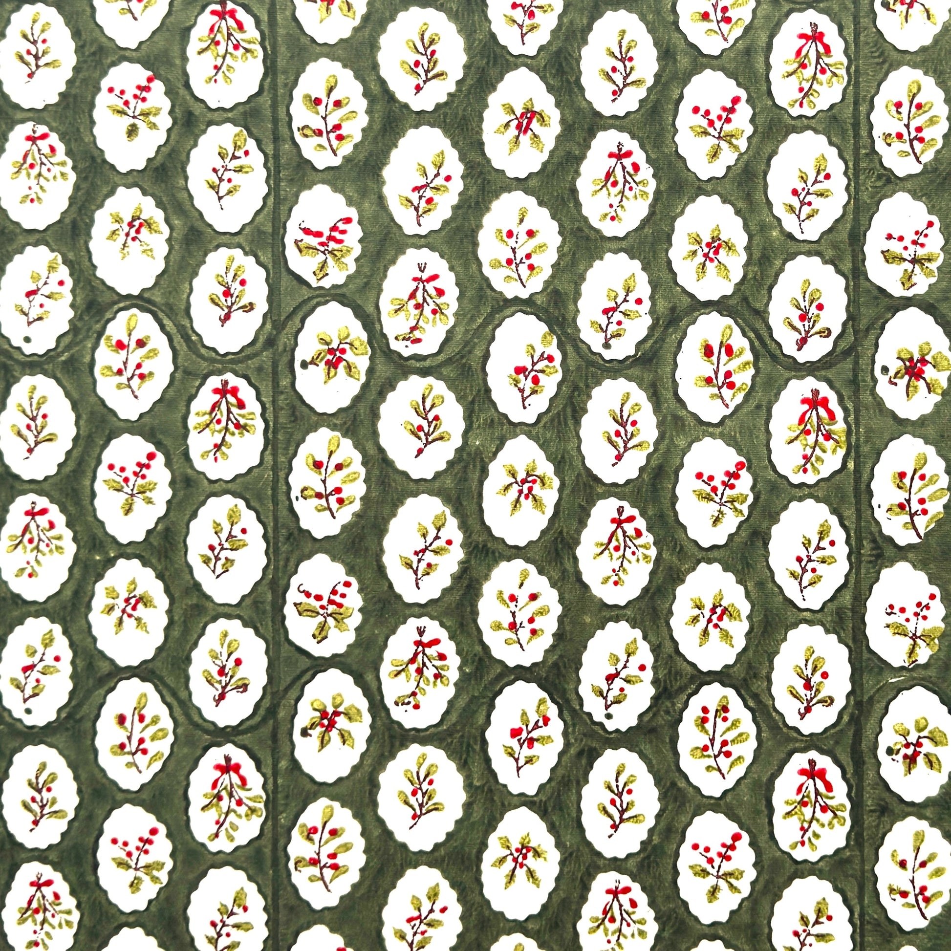 a sheet of block printed paper with a dark green backdrop and white oval scallops with winter foliage motif in the centre