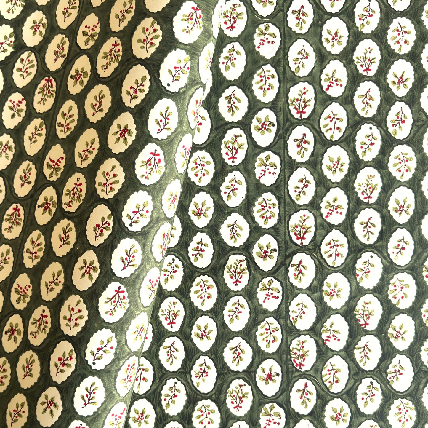 a sheet of block printed paper with a dark green backdrop and white oval scallops with winter foliage motif in the centre