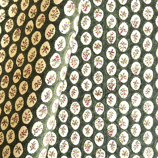 a sheet of block printed paper with a dark green backdrop and white oval scallops with winter foliage motif in the centre